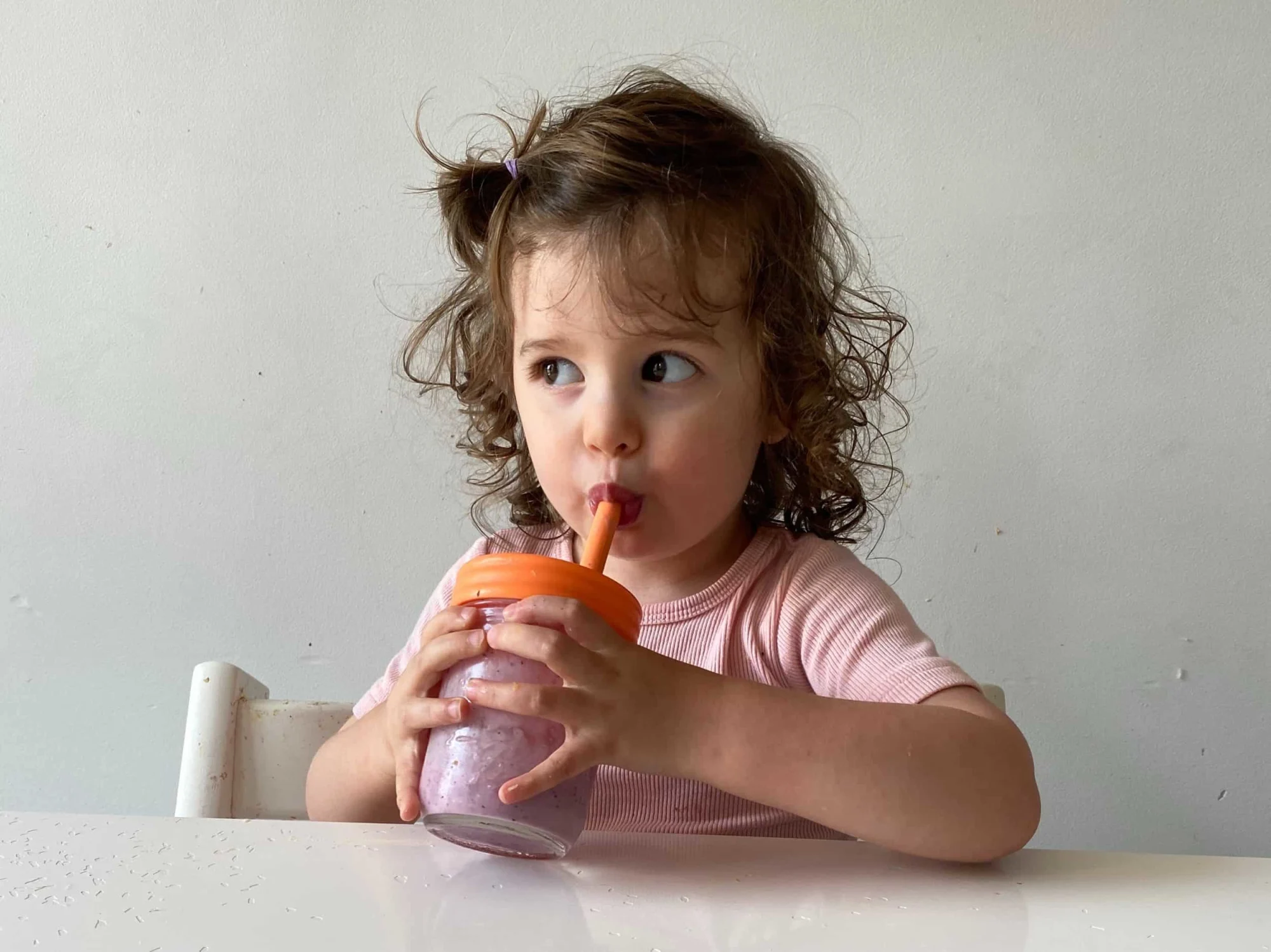 a toddler girl drinks a berry smoothie