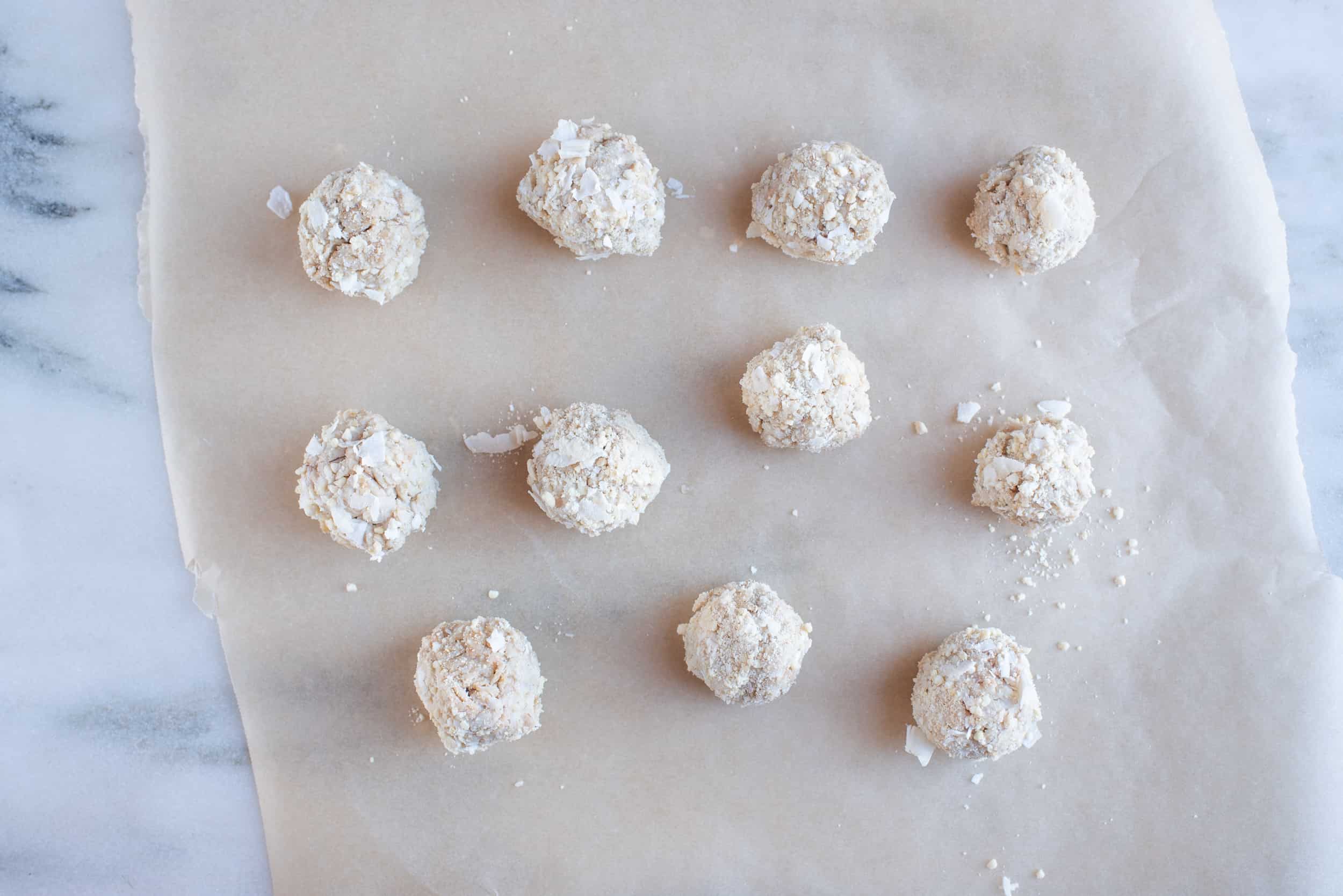 eleven cashew coconut balls on a piece of brown parchment paper on a marble background