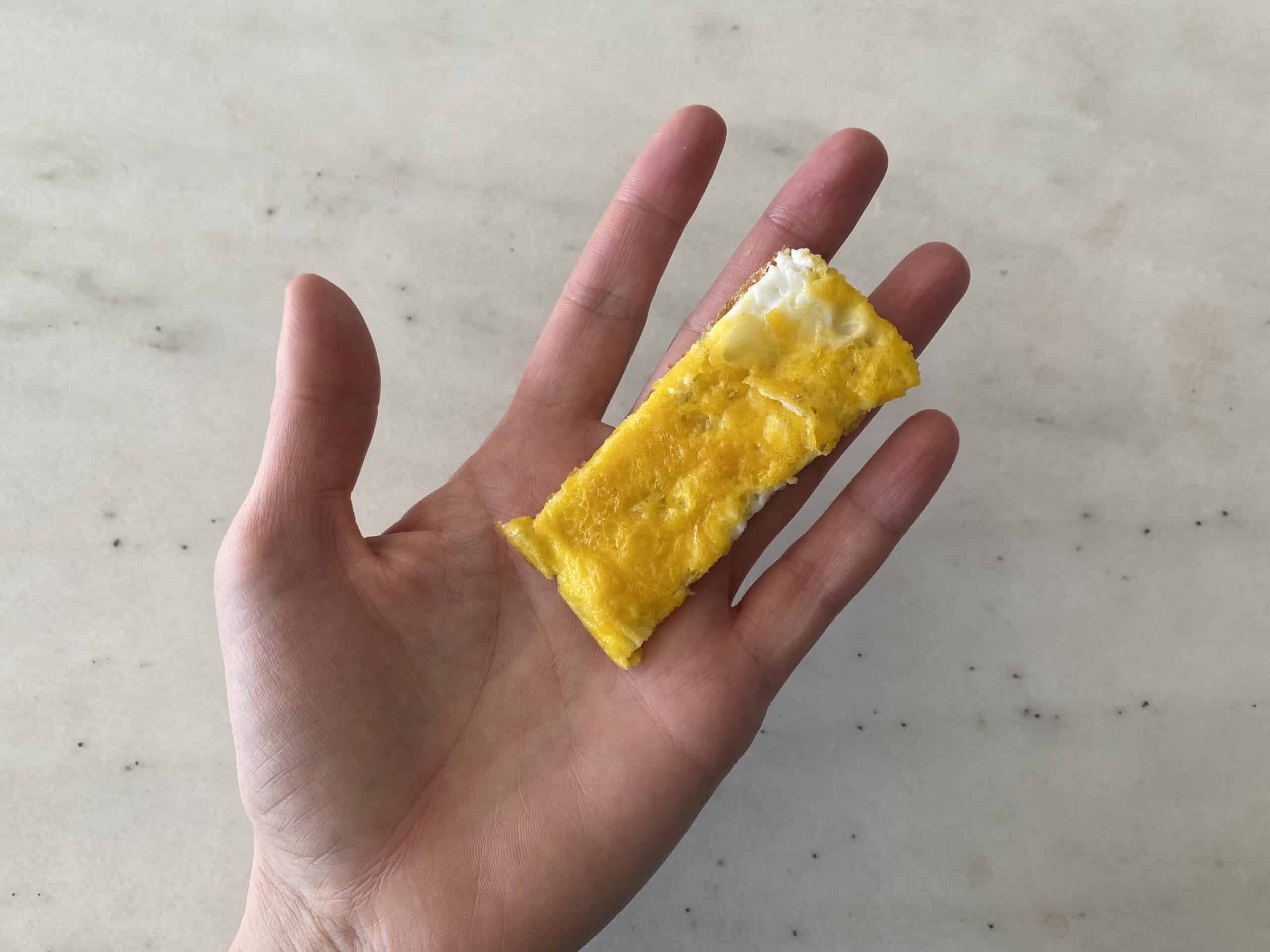 a hand holding a strip of egg omelet for babies 6 months+