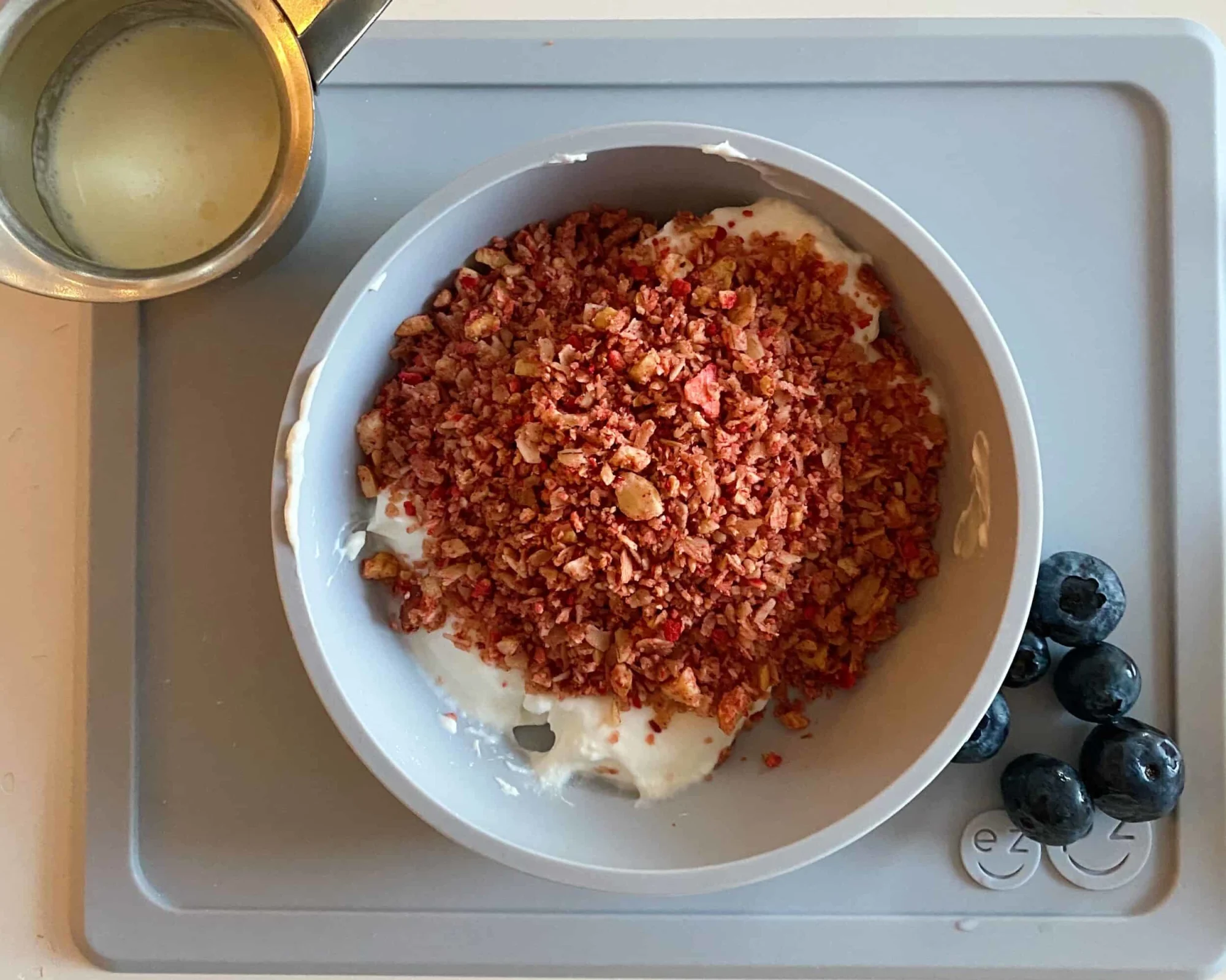 a bowl of strawberry granola, pulverized into a fine meal, with a pitcher of cream on the side