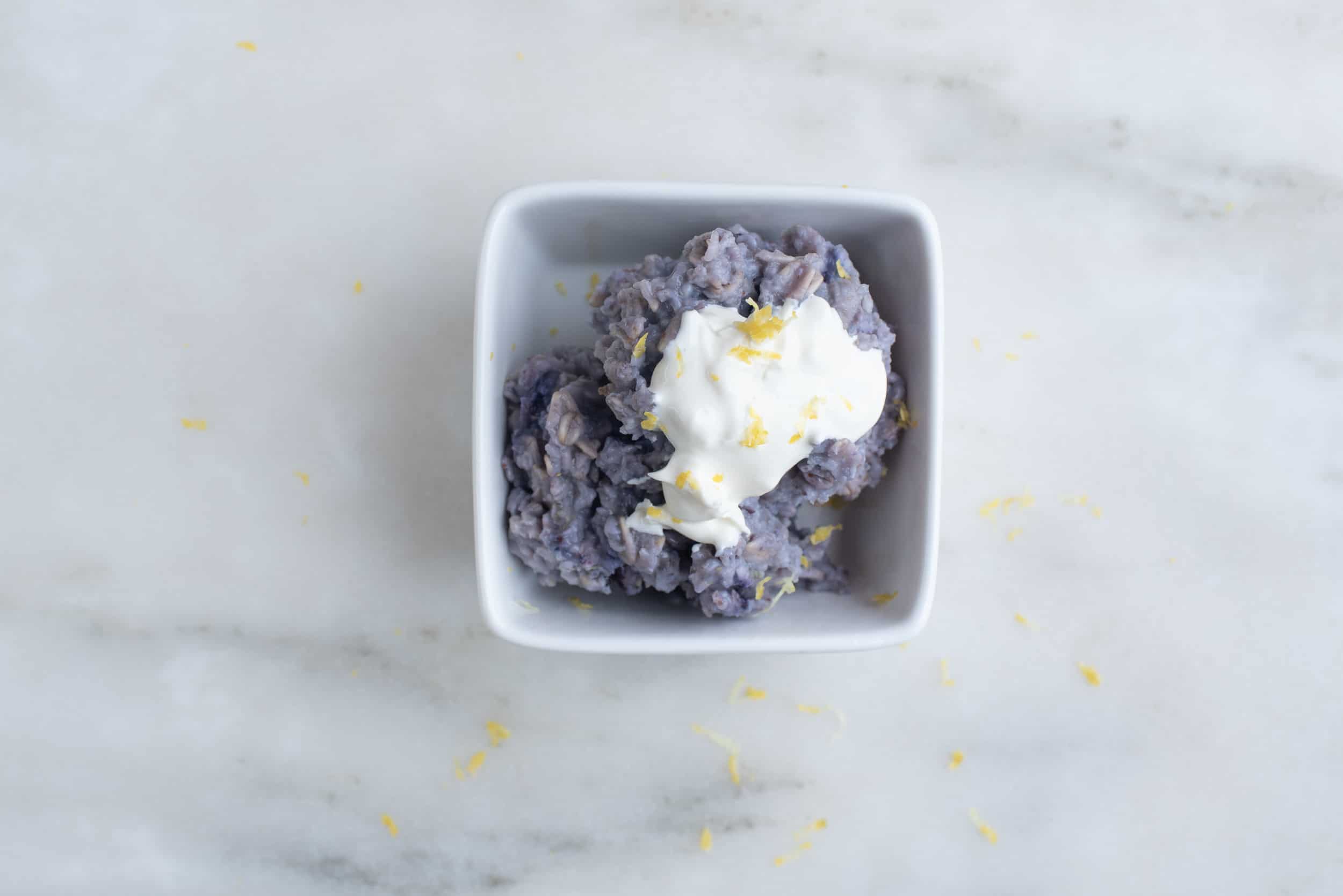 bowl of blueberry oatmeal topped with mascarpone cheese and lemon zest, sitting on a countertop