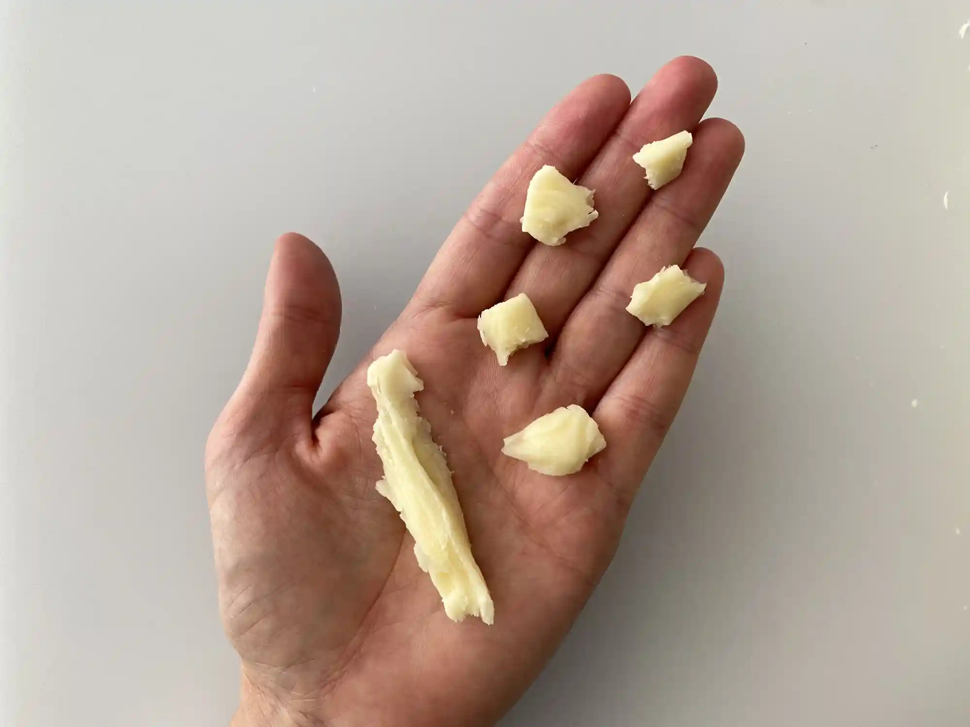 a hand holding one long skinny piece of quesillo next to five small bite-sized pieces of quesillo for babies 9 months+