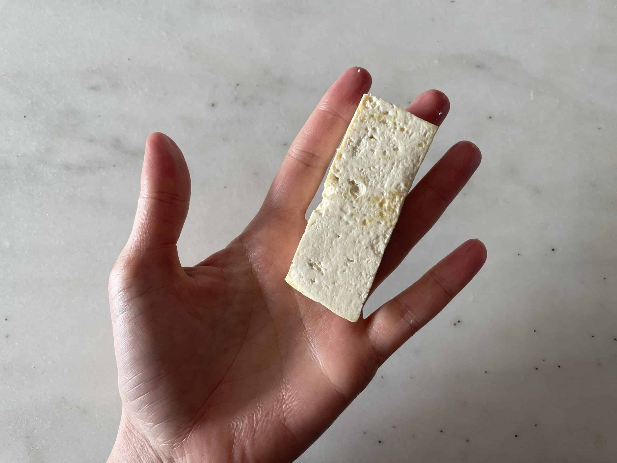 a hand holding a strip of cooked tofu the width of two fingers for babies starting solids