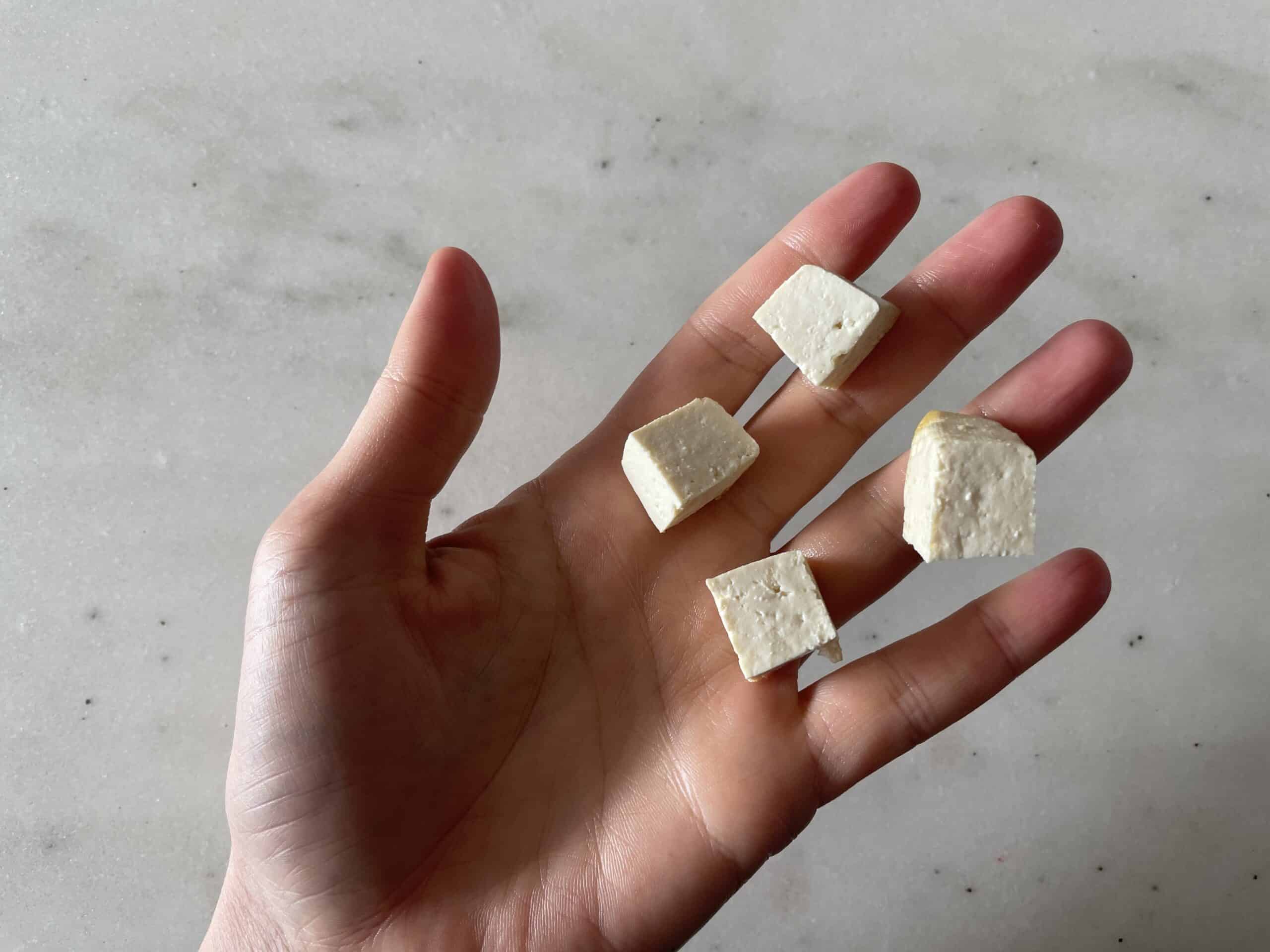 a hand holding bite-sized pieces of cooked tofu for toddlers 12 months+