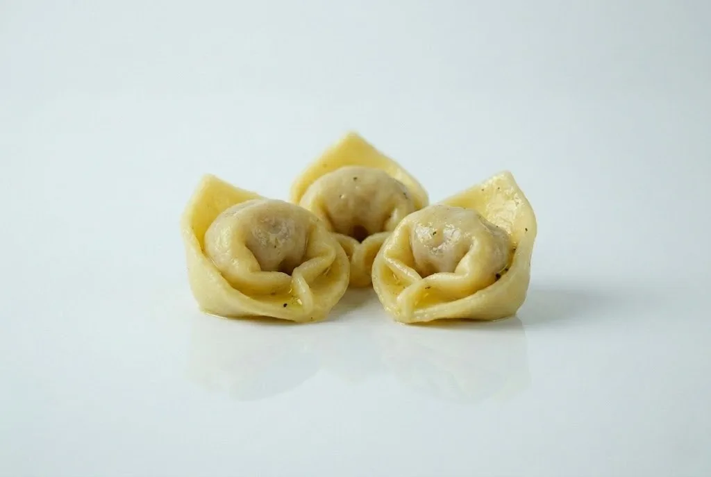 Three pieces of cooked tortellini are arranged on a white surface, each with folded edges and visible filling inside.