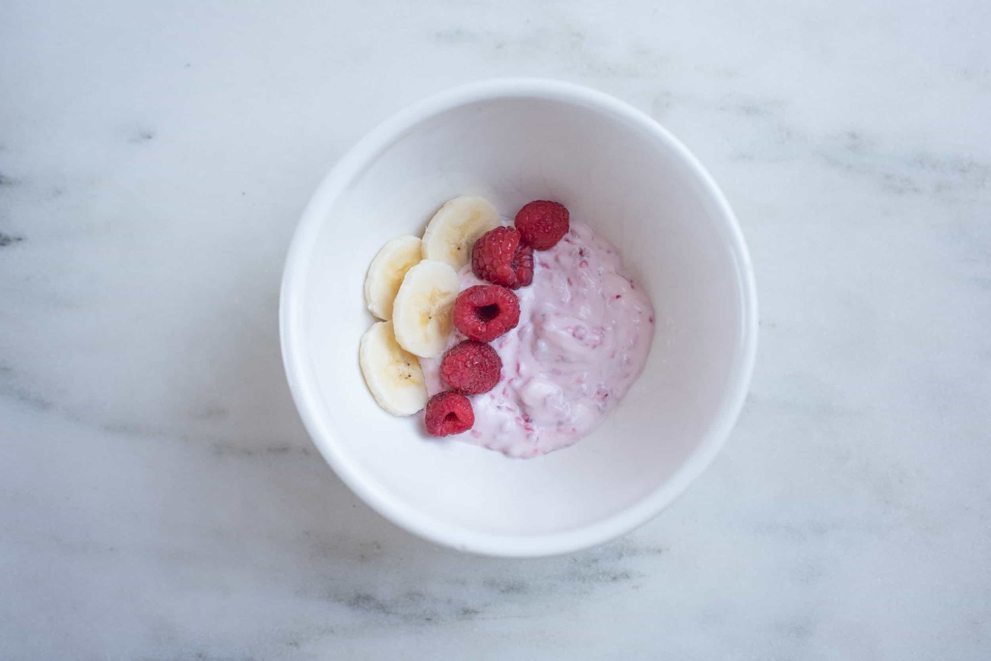 bowl of smashed raspberries with Greek yogurt, topped with whole raspberries and banana slices