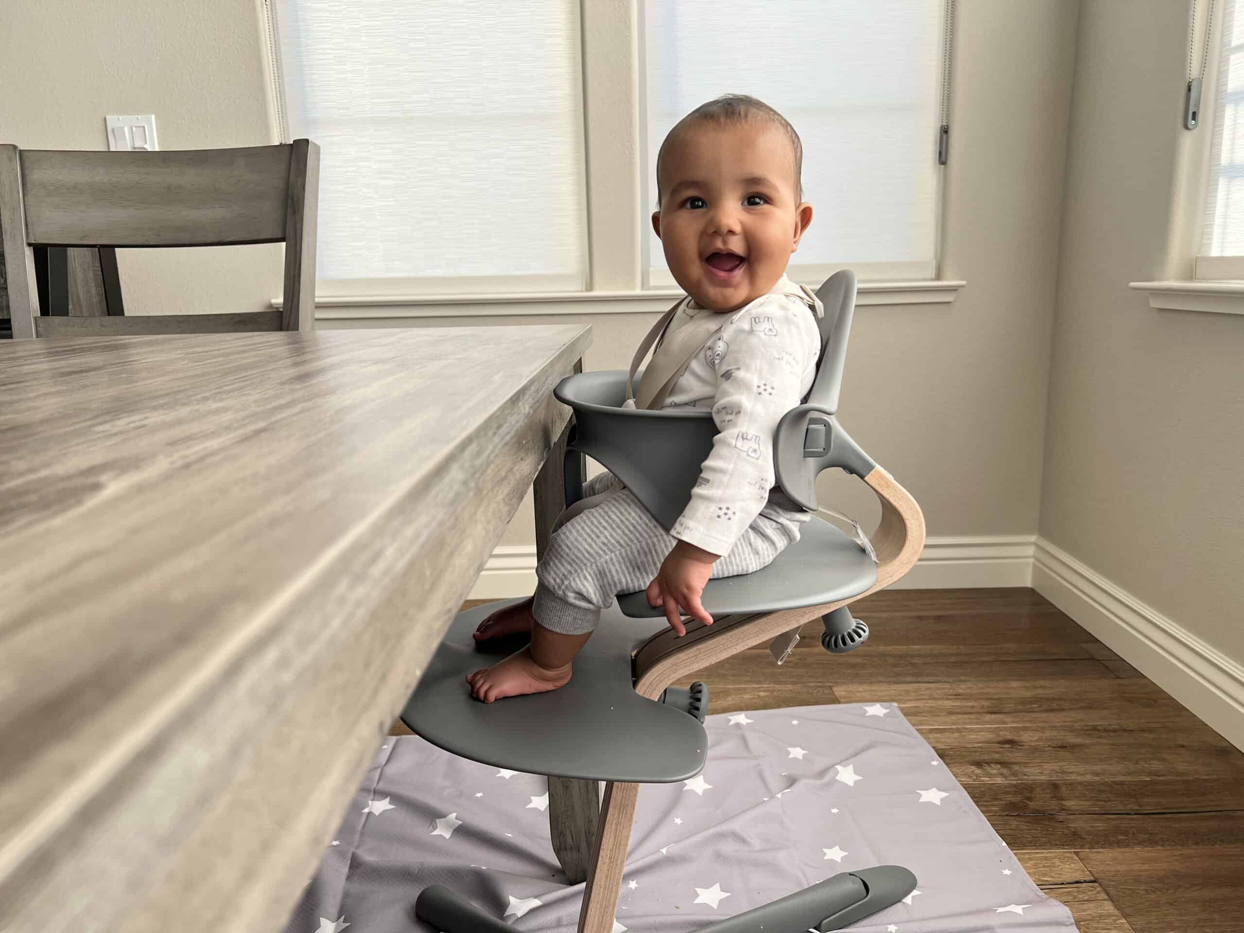 a baby sitting upright in a high chair next to a table