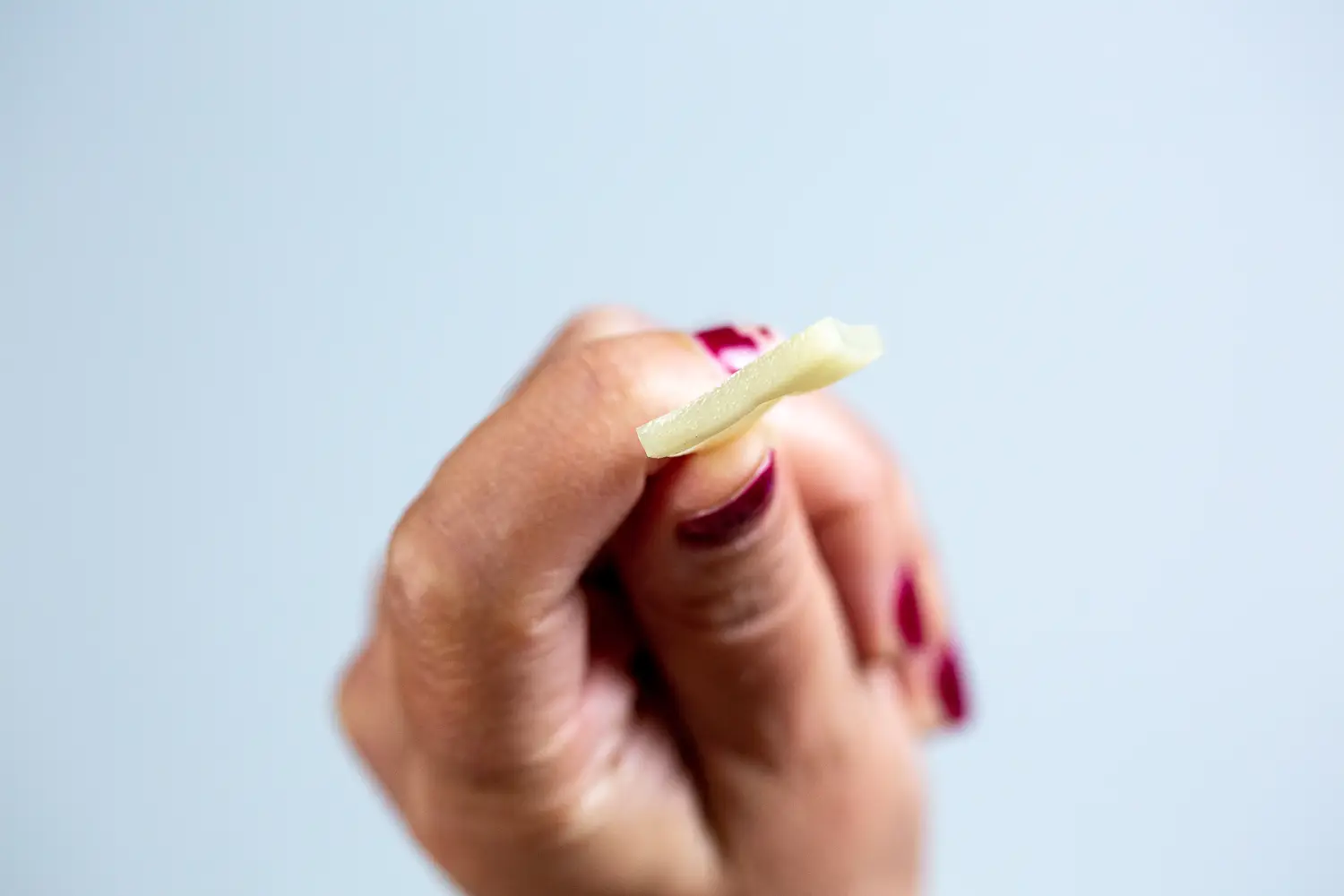 a hand holding a bite-sized piece of emmentaler cheese between thumb and forefinger to show how thin it is