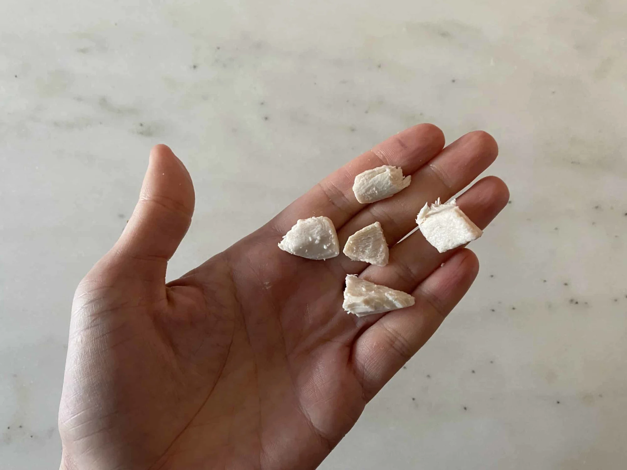 a hand holding five bite-sized pieces of chicken for children 12 months +