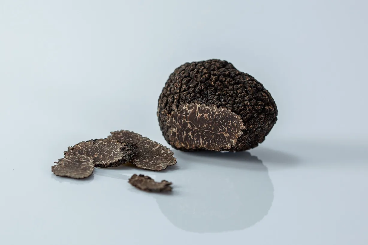 a whole black truffle next to some thin slices of truffle on a white background