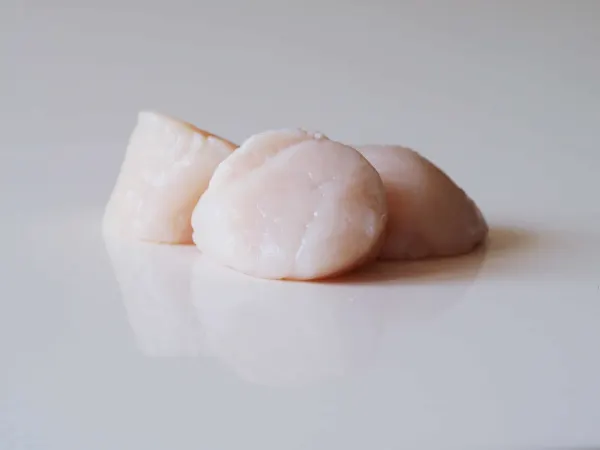 a photograph of three raw scallops ready to be cooked on a white background