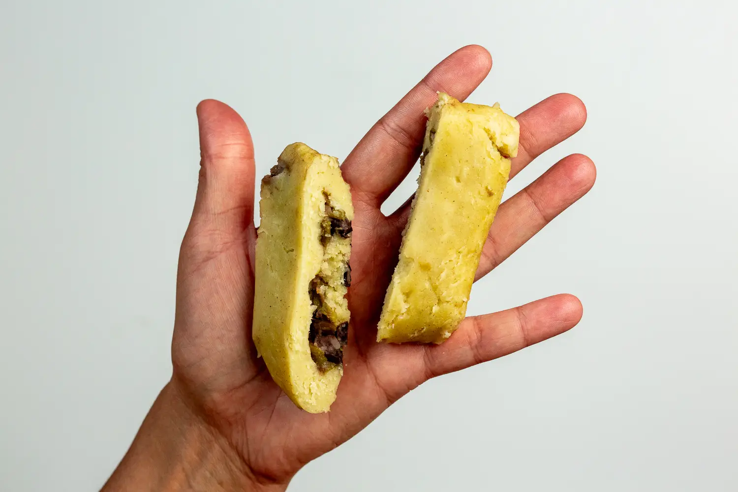 a photograph of a hand holding two short strips of tamales