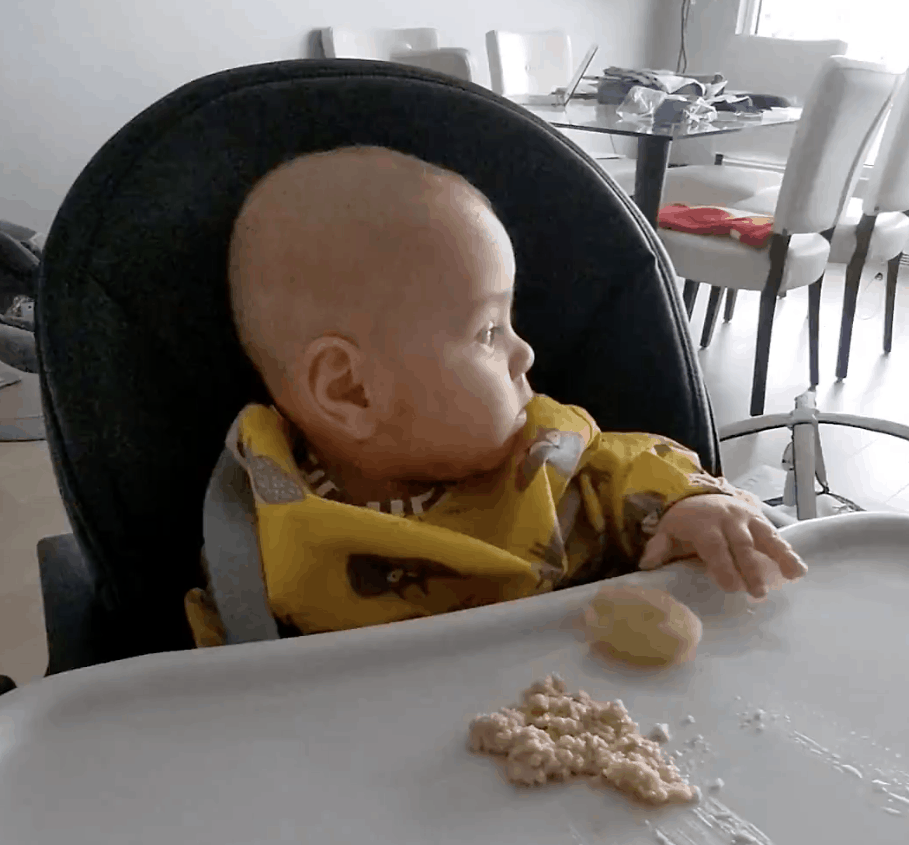 a baby in a high chair looks away from his food, uninterested in eating