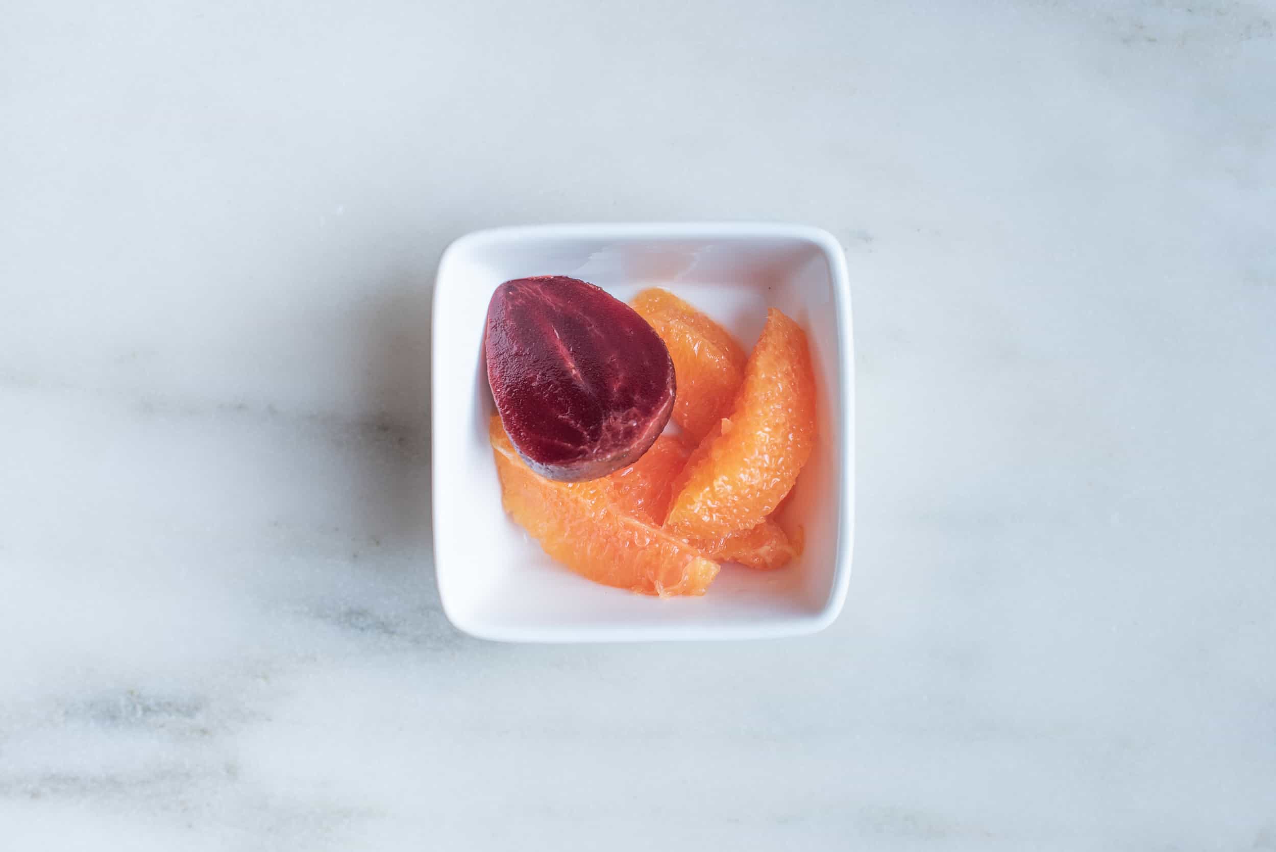 a square white bowl with four large supremed orange wedges and a cooked beet half for babies starting solids