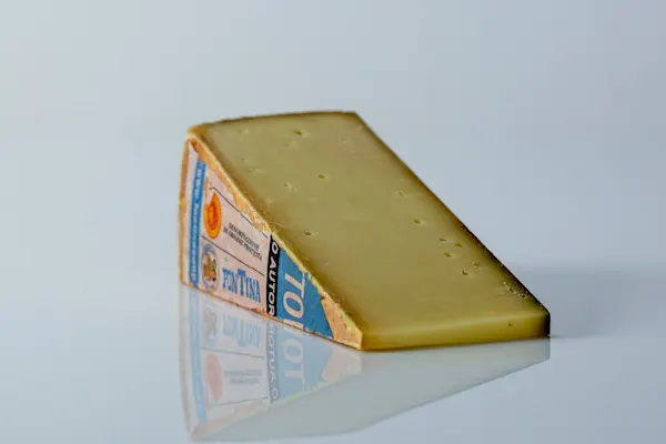 a photograph of a wedge of fontina cheese on a white reflective surface