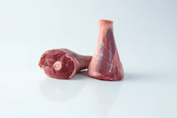 a photograph of two raw lamb shanks on a white background