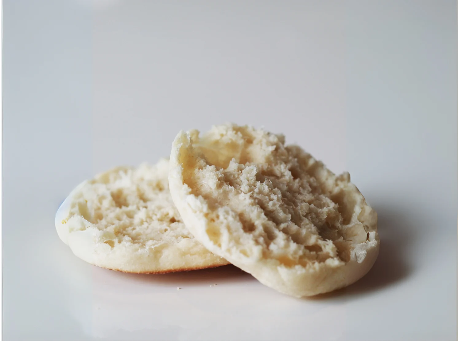 a photograph of a cut untoasted english muffin on a white background