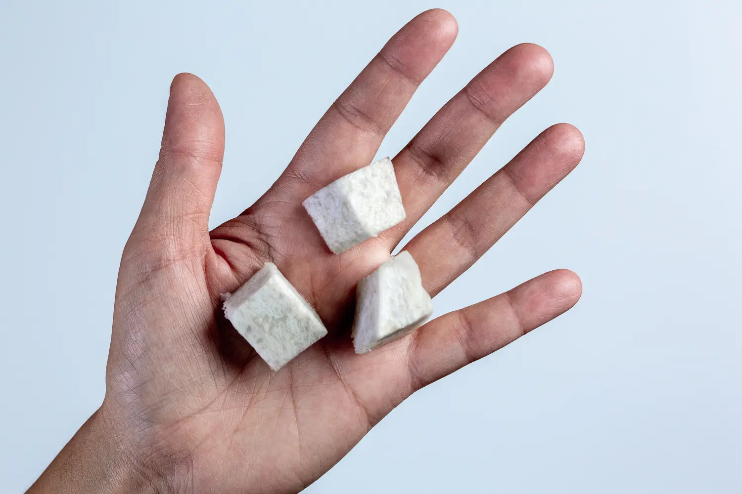 a hand holding three bite-sized pieces of cooked soft taro in the palm