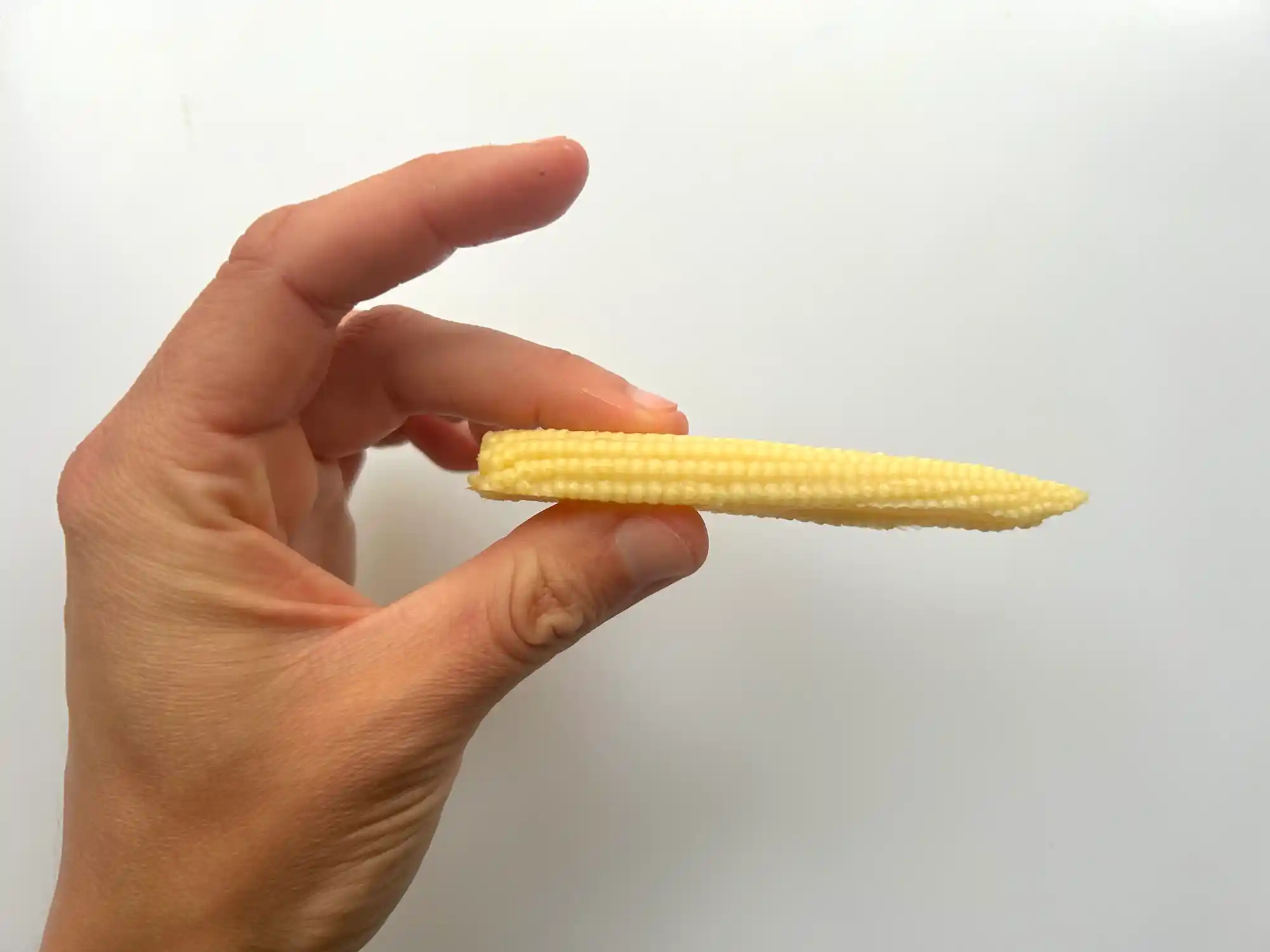 Baby corn cut lengthwise side view hand pic a photograph of a hand holding a piece of baby corn cut lengthwise