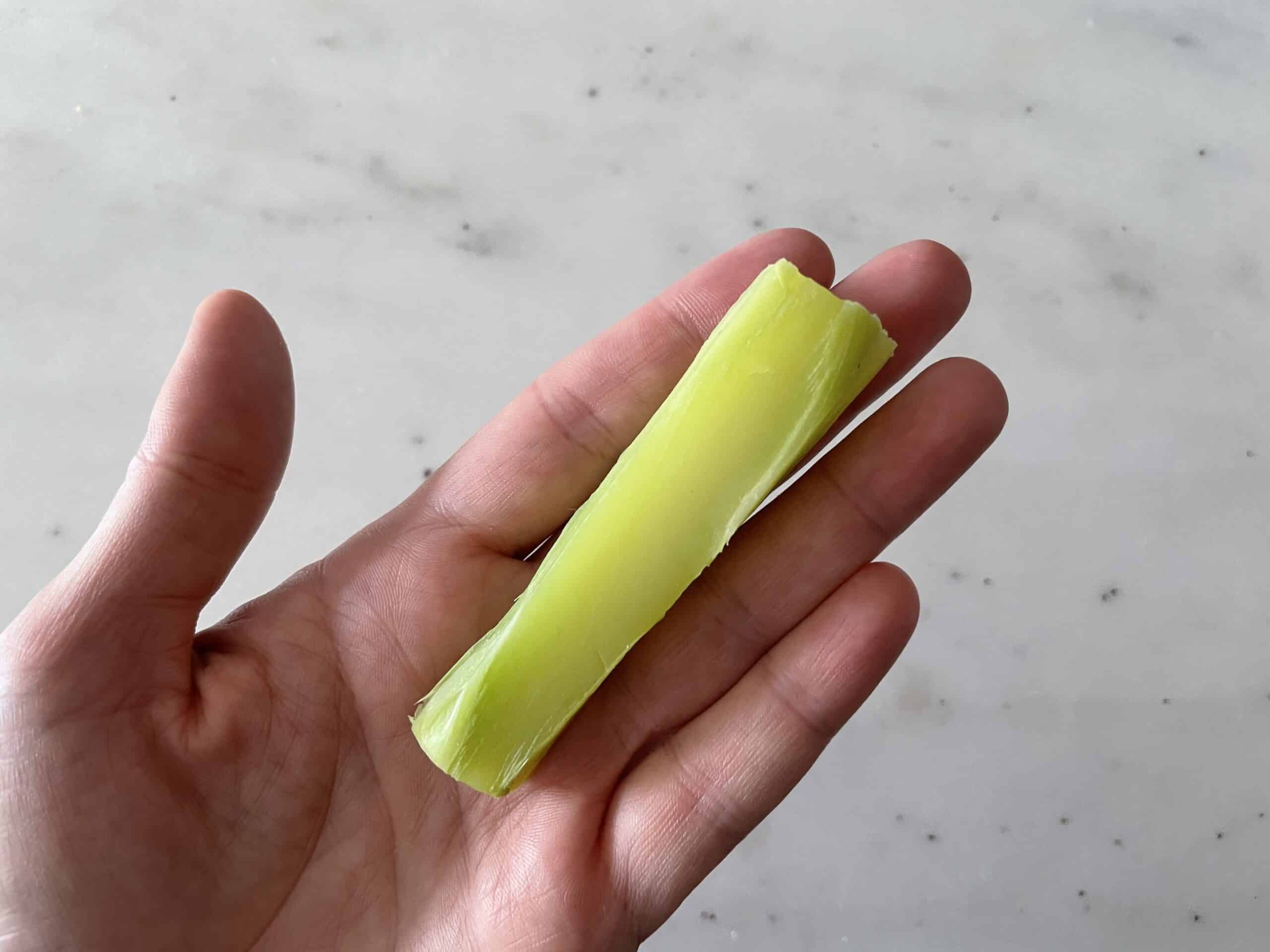 a hand holding one steamed broccoli stem, cut in half lengthwise, for babies 6 months+