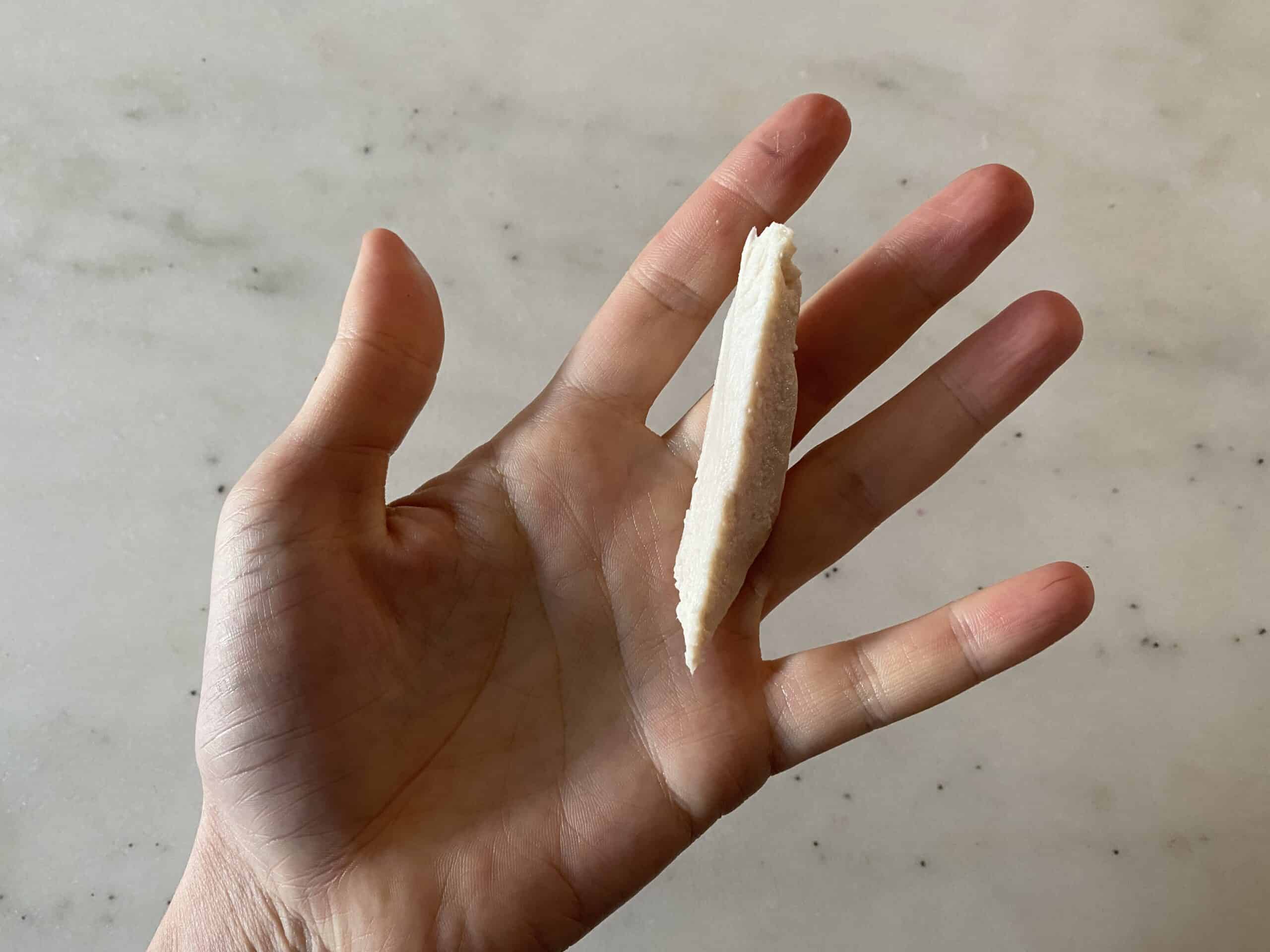 a hand holding a thin slice of chicken for babies 8 months+