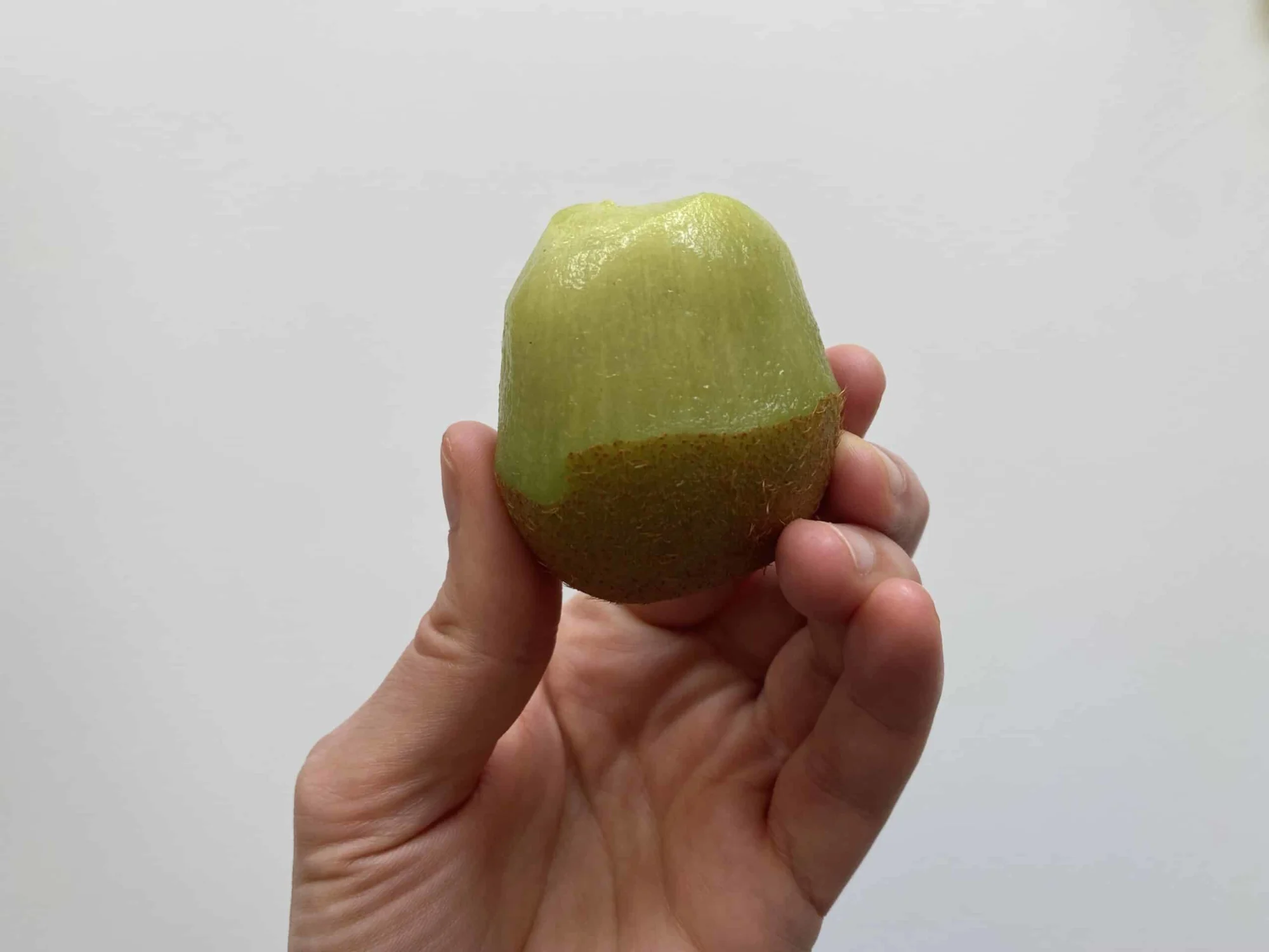 a hand holding a whole kiwi with only the top peeled for babies starting solids