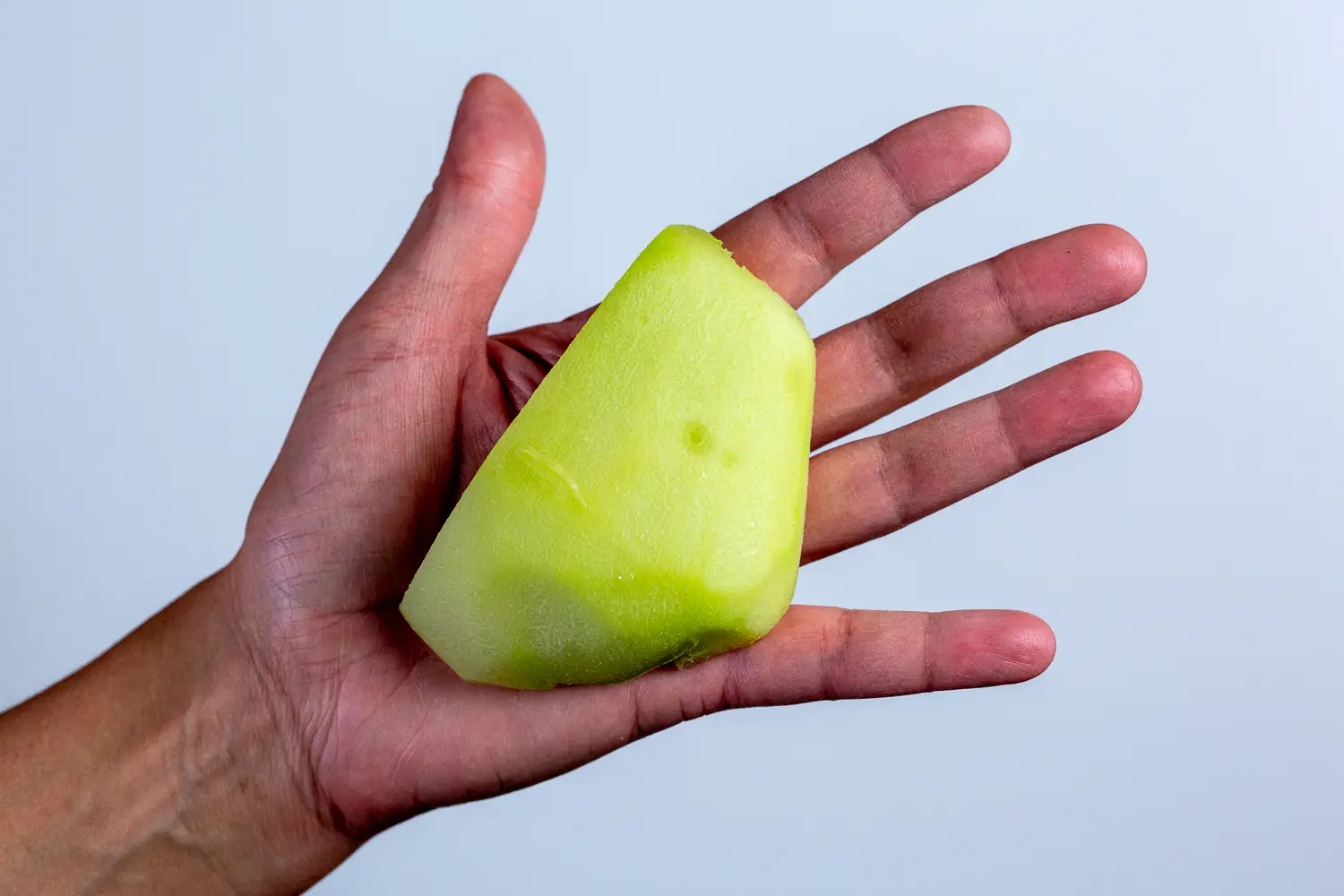 a photograph of a hand holding a large wedge of cooked chayote for babies 6 months +