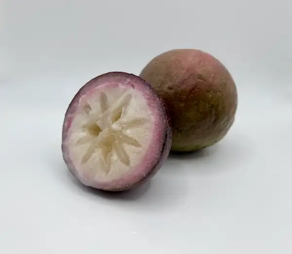 a photograph of a star apple cut in half in front of a whole star apple on a white background