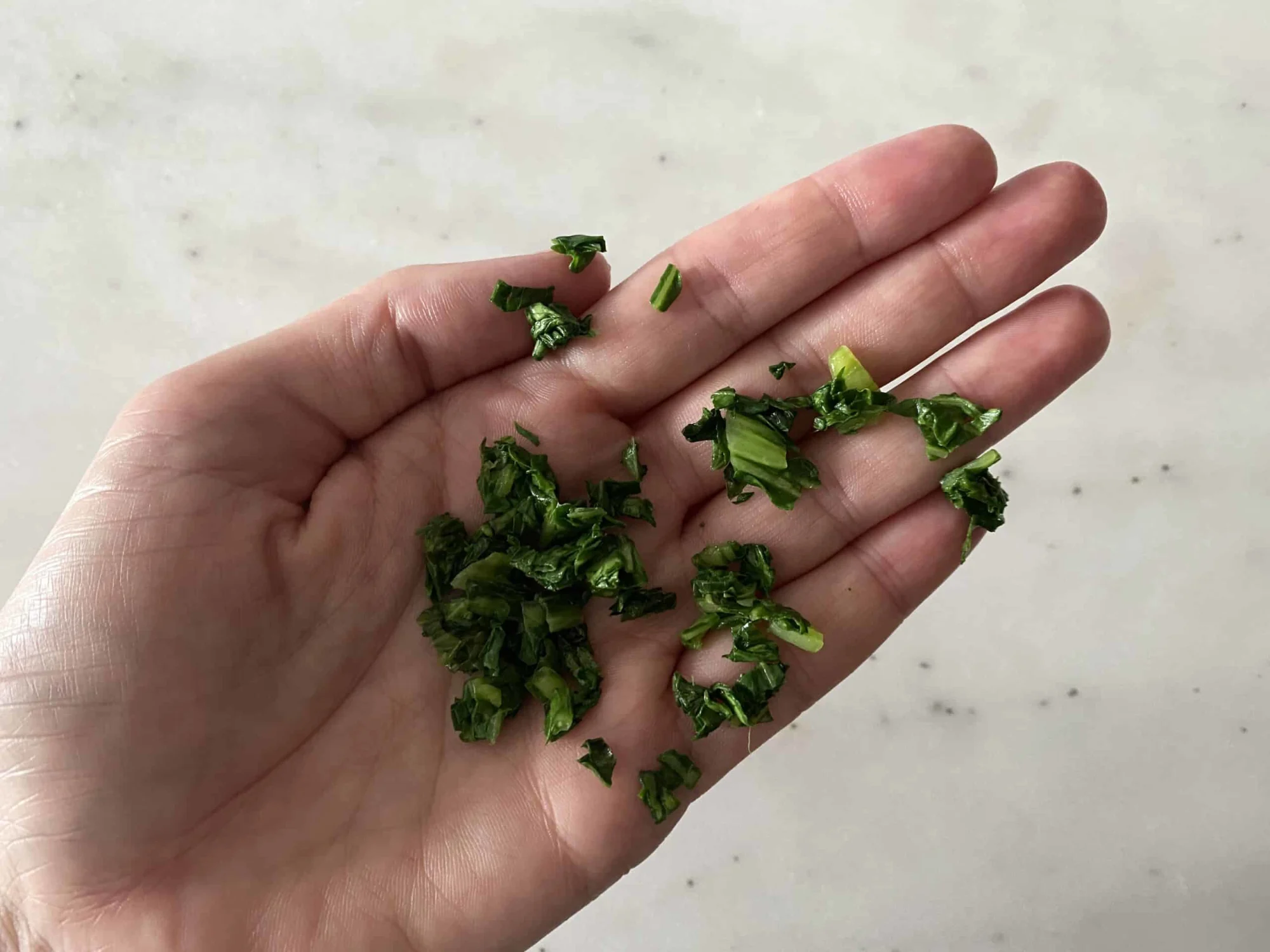 Minced cooked bok choy leaves in the palm of an adult hand