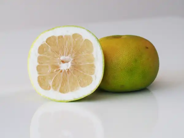 a whole pomelo next to a pomelo cut in half on a white background