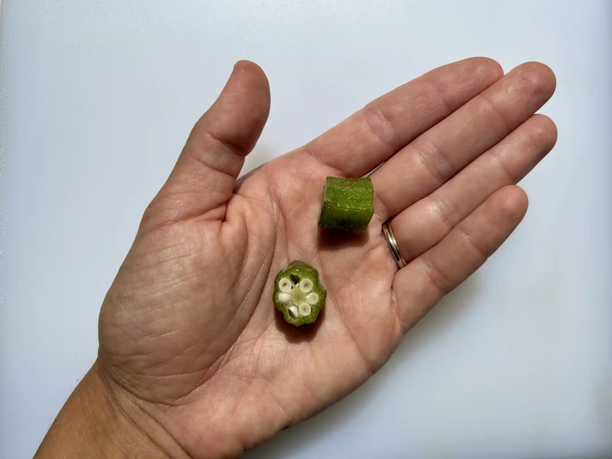 a photograph of a hand holding two bite-sized pieces of cooked okra