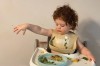 toddler sitting on a white high chair and tray, throwing food off the table tray to the floor