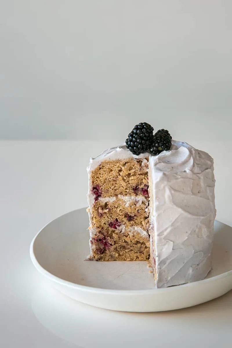 A cut blackberry parsnip cake reveals three pale layers with dark flecks and white frosting.