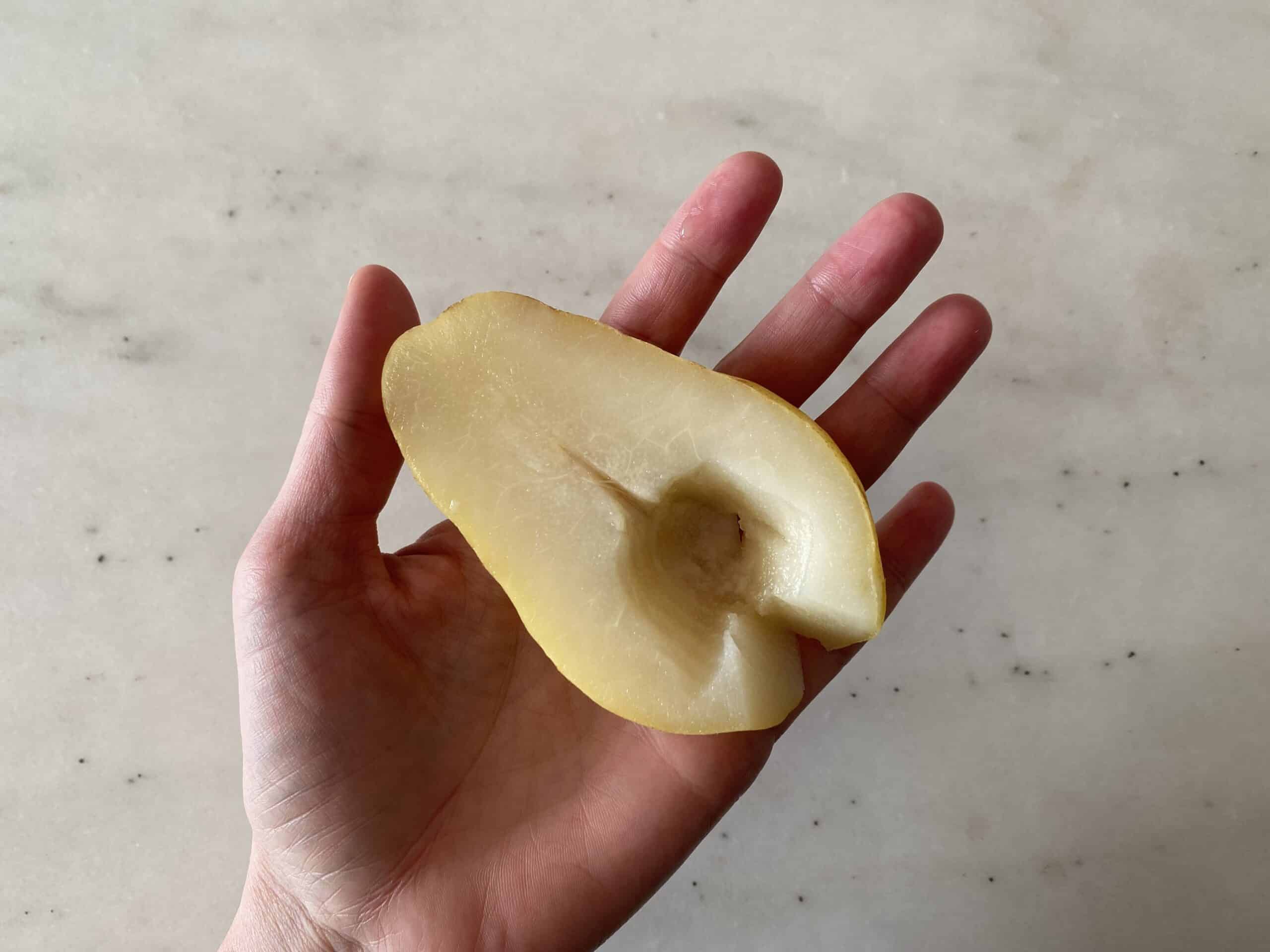 a hand holding a cooked pear half for babies starting solids