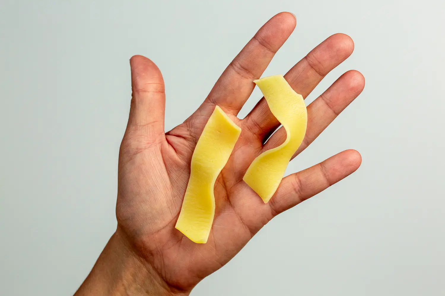 a hand holding two short pieces of wide, flat noodles