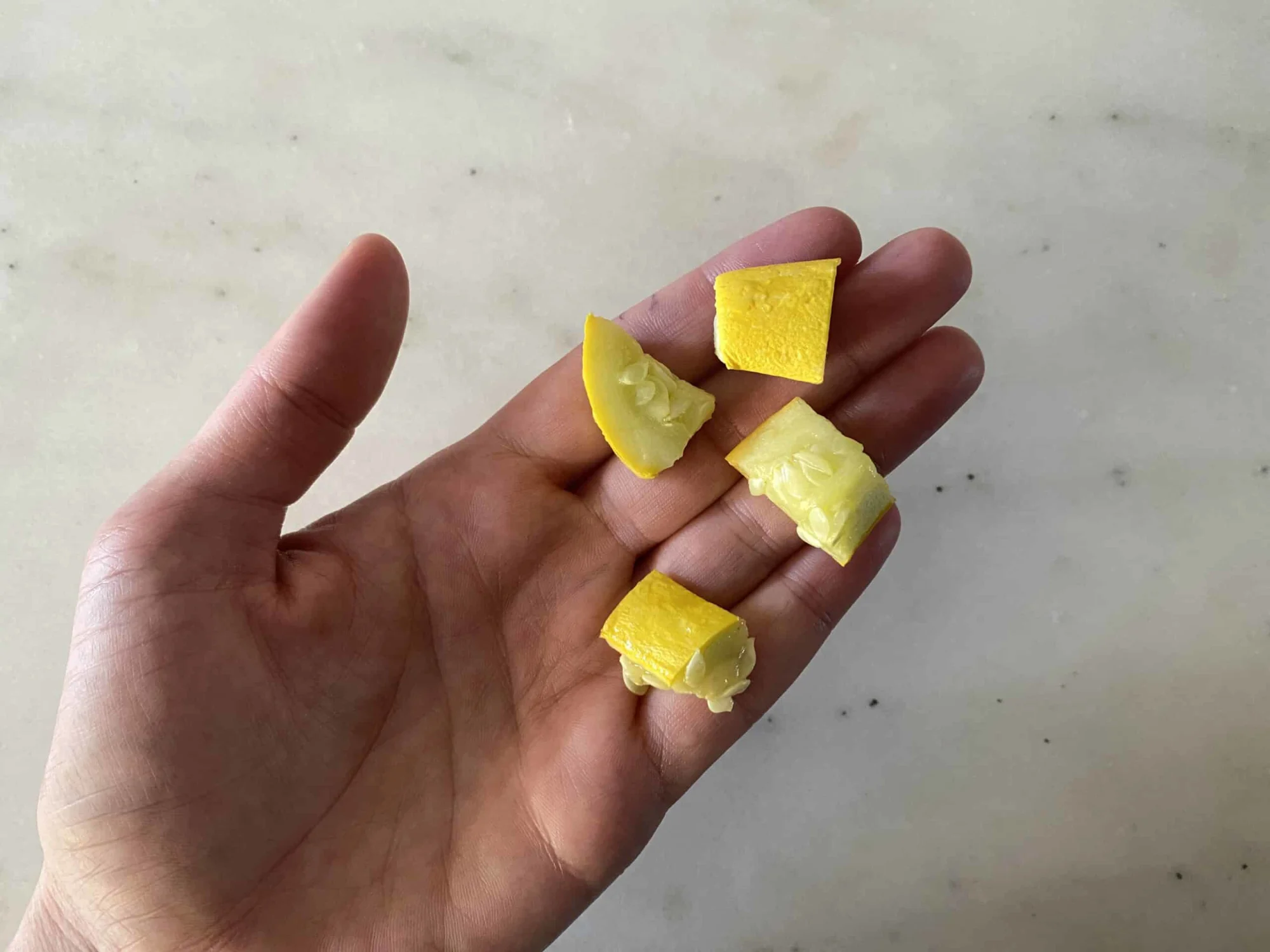 a hand holding four bite-sized pieces of cooked summer squash for babies 9 months +