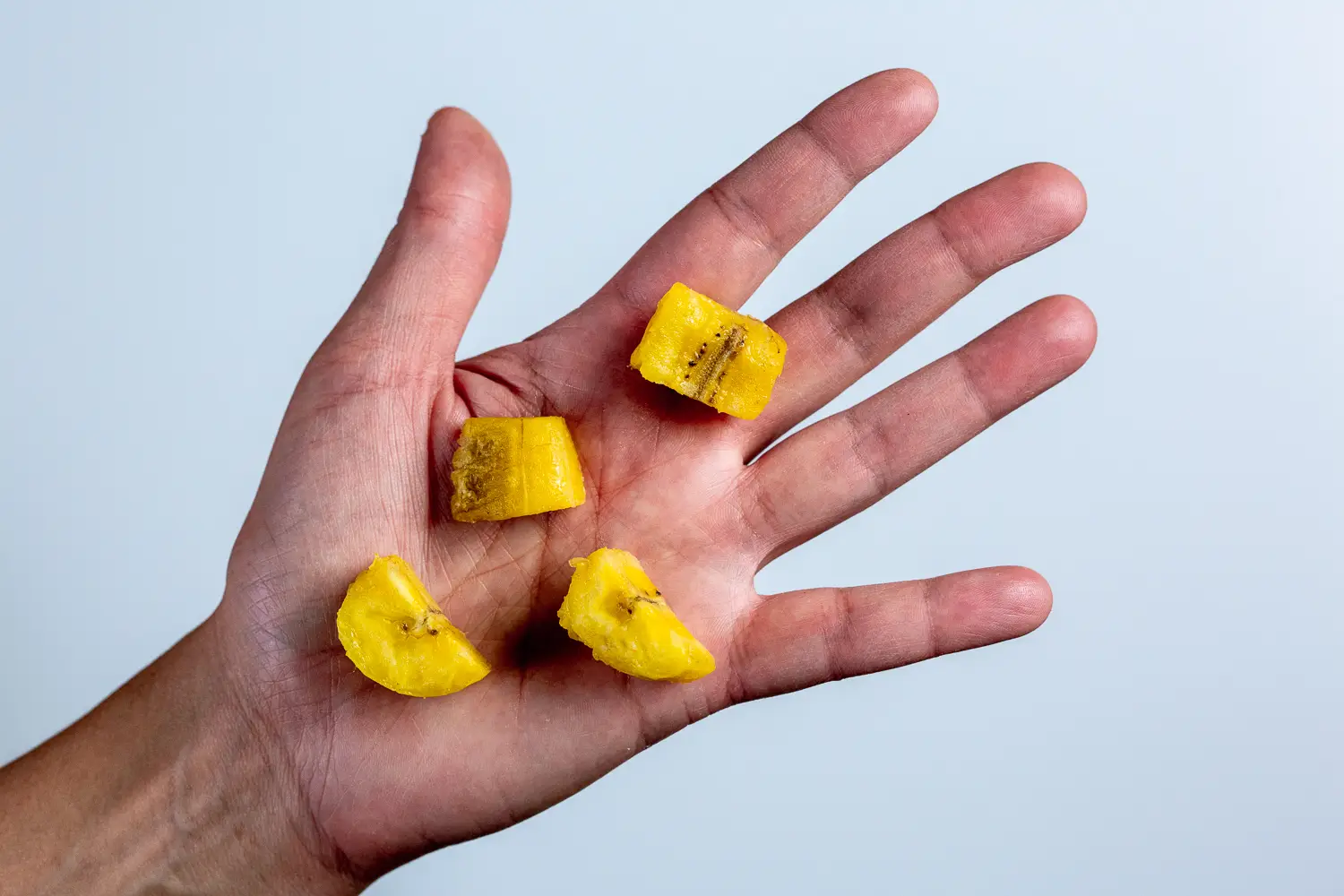 a photograph of a hand holding four bite-sized pieces of cooked plantain