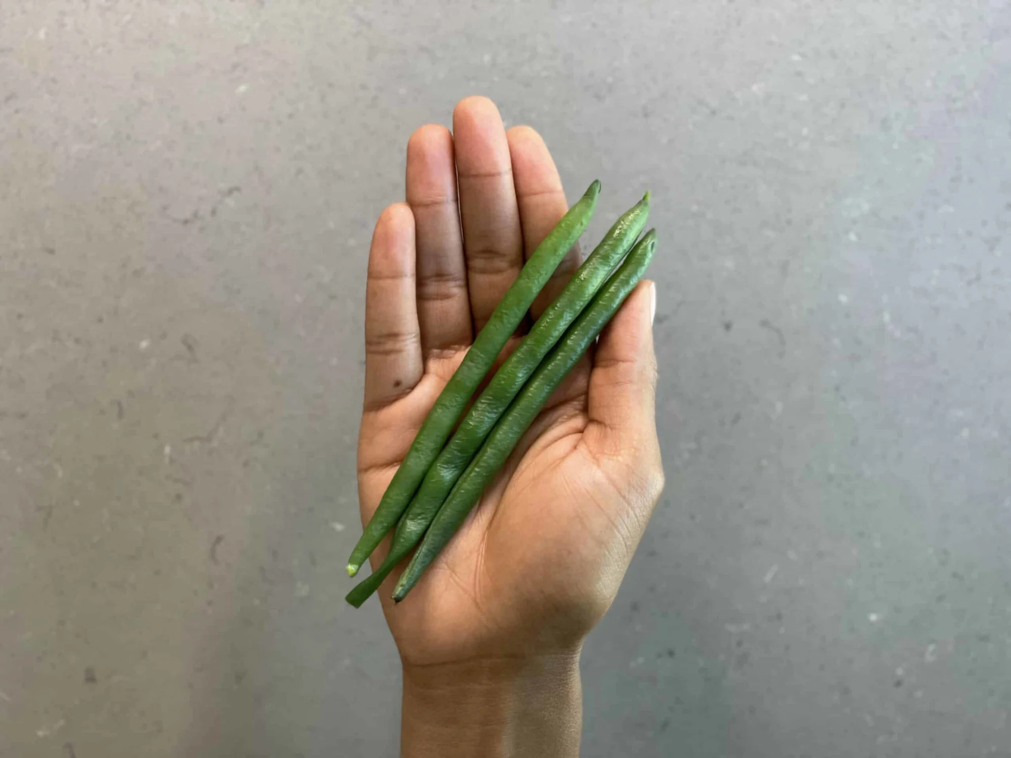a hand holding three whole cooked green beans for babies 6 months+