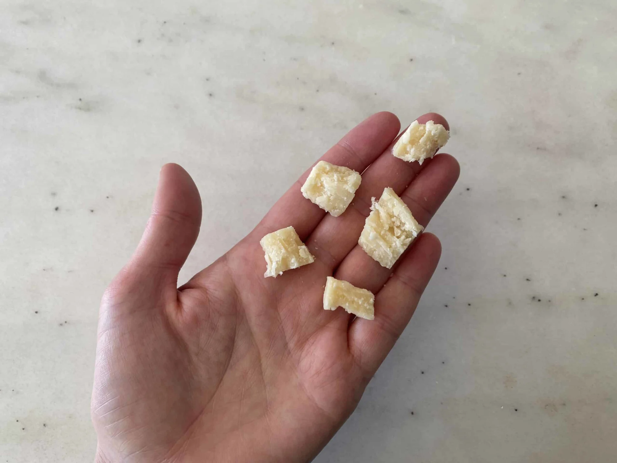 a hand holding five bite sized pieces of parmesan cut from a thin slice