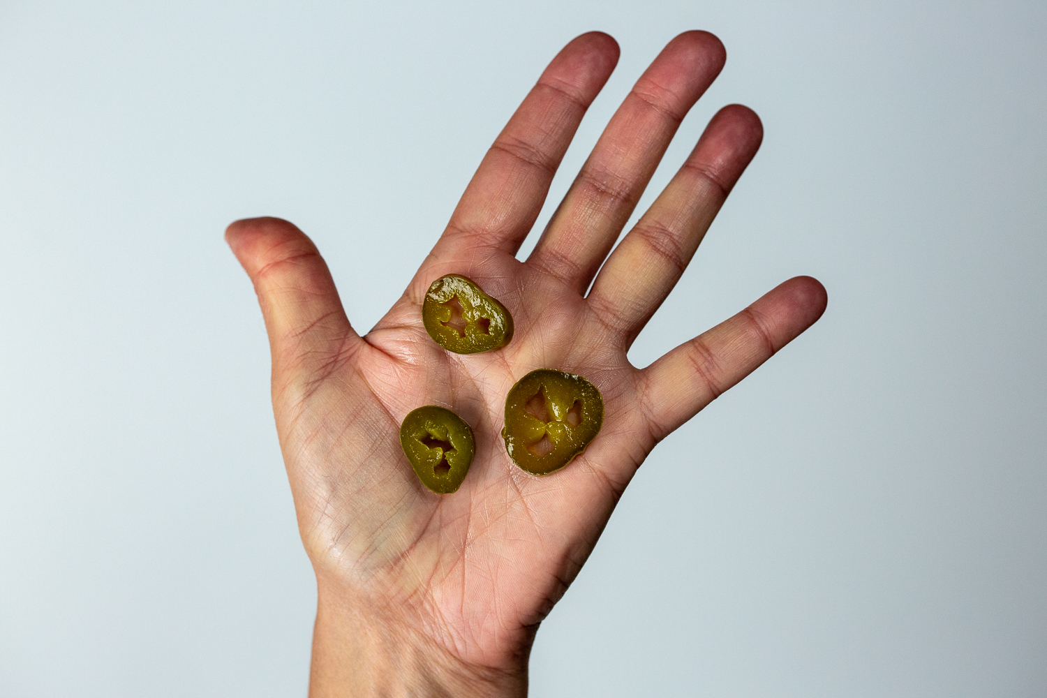 a hand holding three thin slices of jalapeno pepper