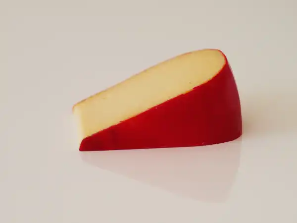 a wedge of edam cheese with a red wax rind on a white background