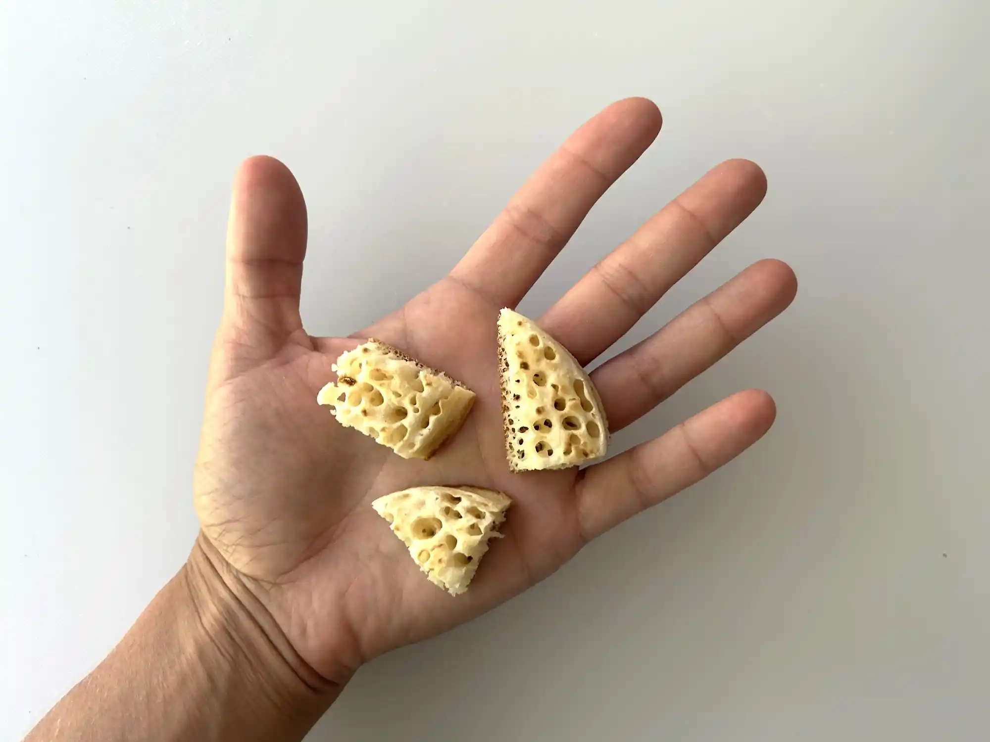 a photograph of a hand holding three bite-sized pieces of toasted crumpet