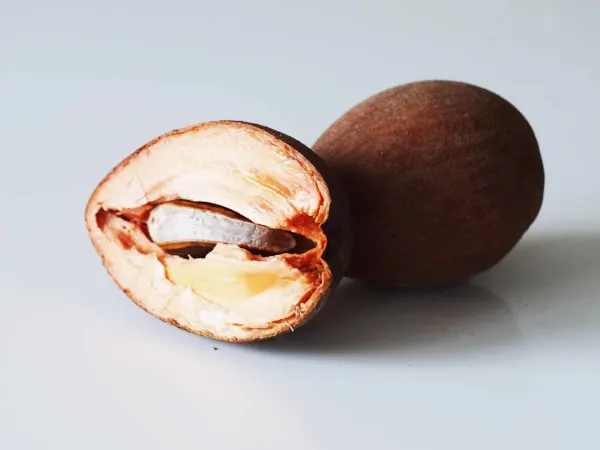 a whole zapote behind a zapote cut in half, showing the seed, on a white background