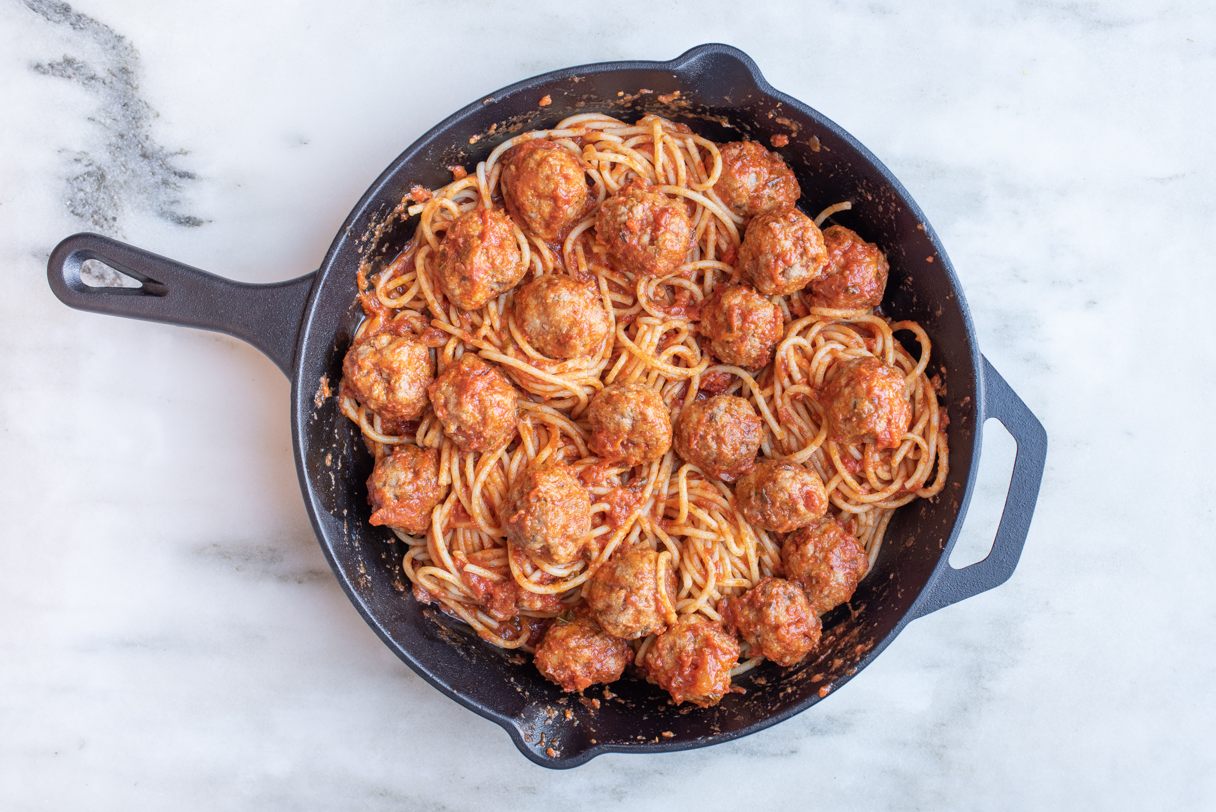 a large cast iron skillet filled with spaghetti and lamb meatballs coated in tomato sauce