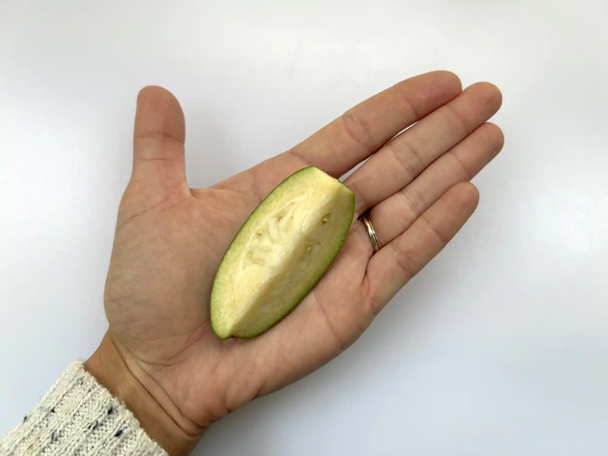 a photograph of a hand holding a large wedge of ripe feijoa with the skin still on