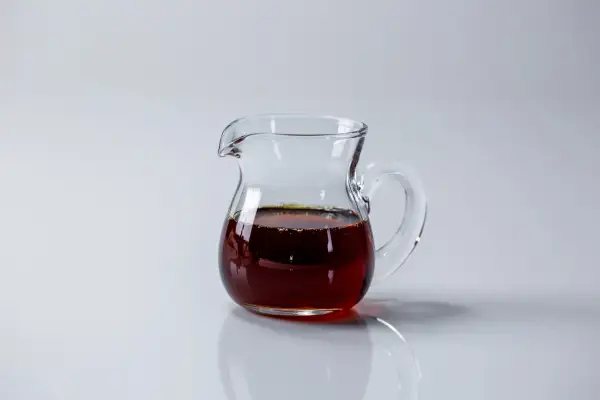 a small clear pitcher half full of amber maple syrup on a white background
