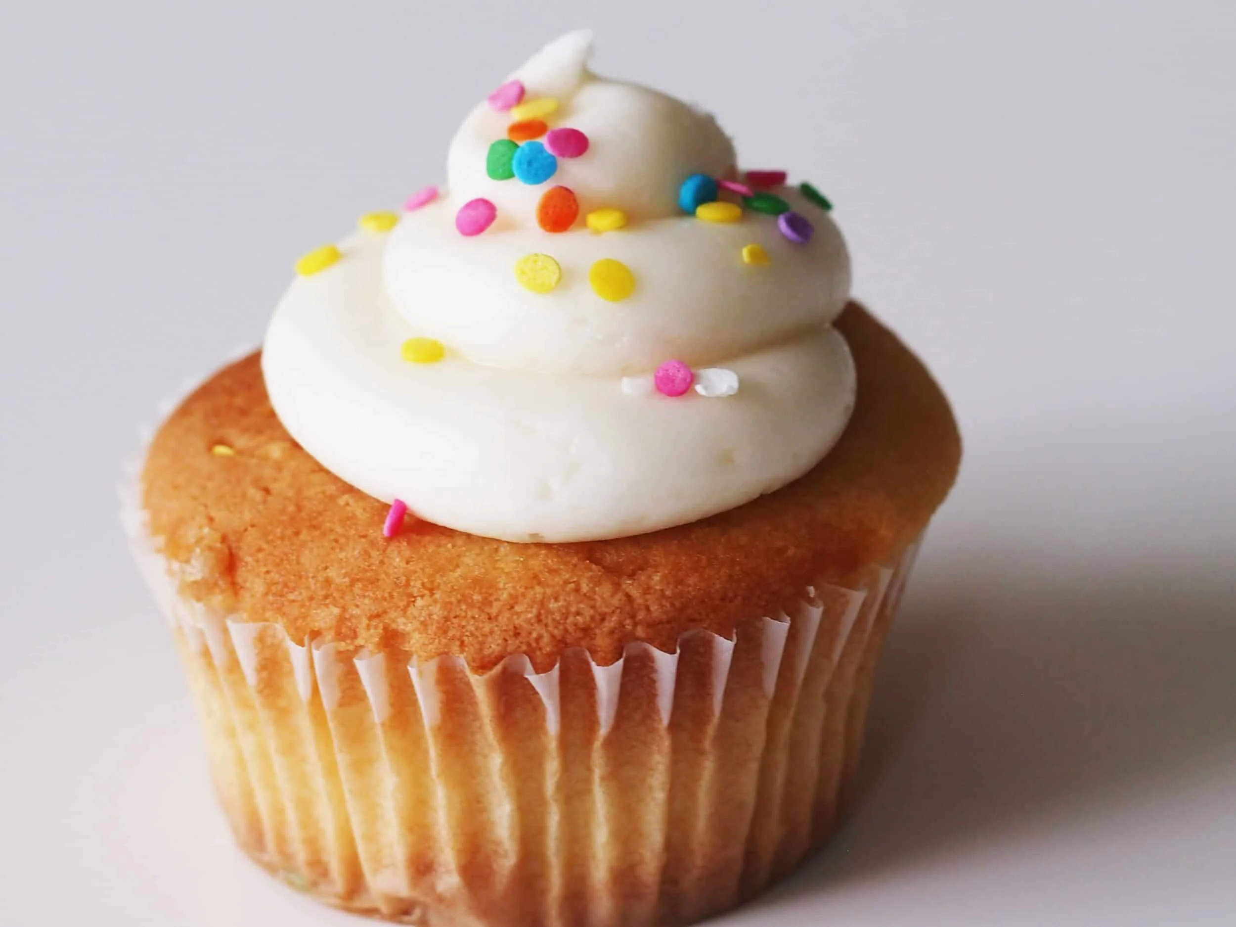 A white cupcake with vanilla frosting and rainbow sprinkles