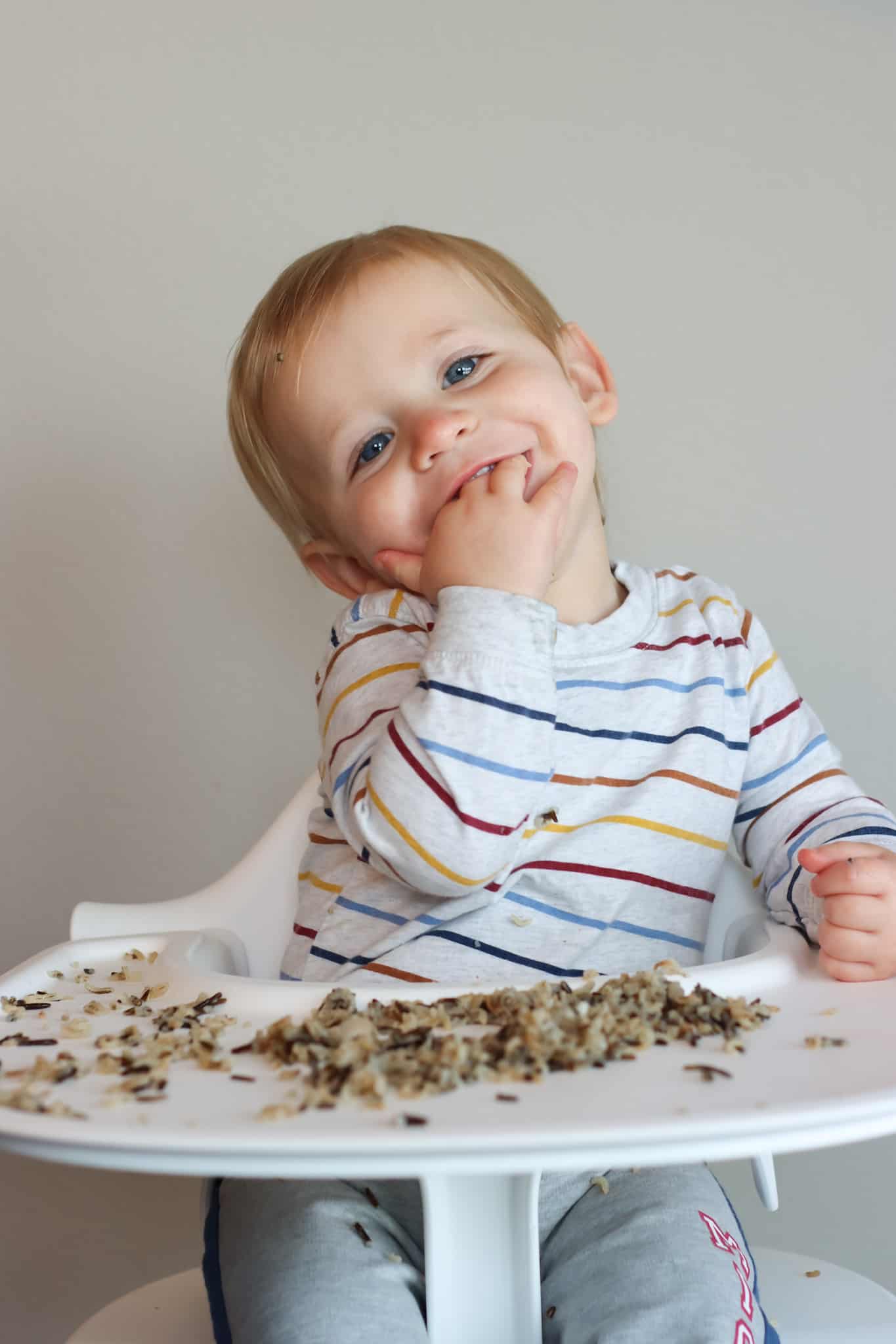 a toddler eating wild rice from a highchair tray