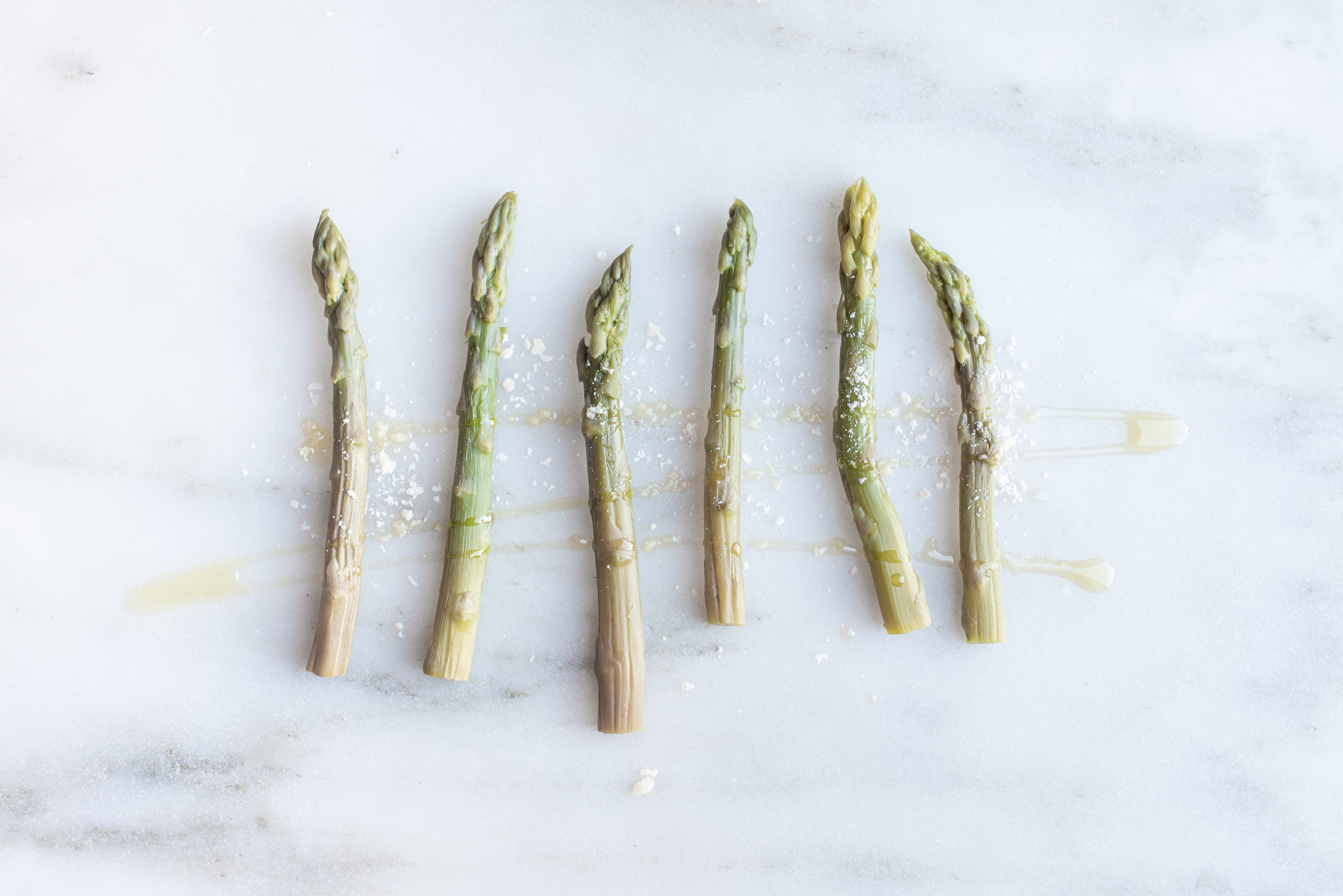 five cooked asparagus spears sprinkled with parmesan cheese on a marble background