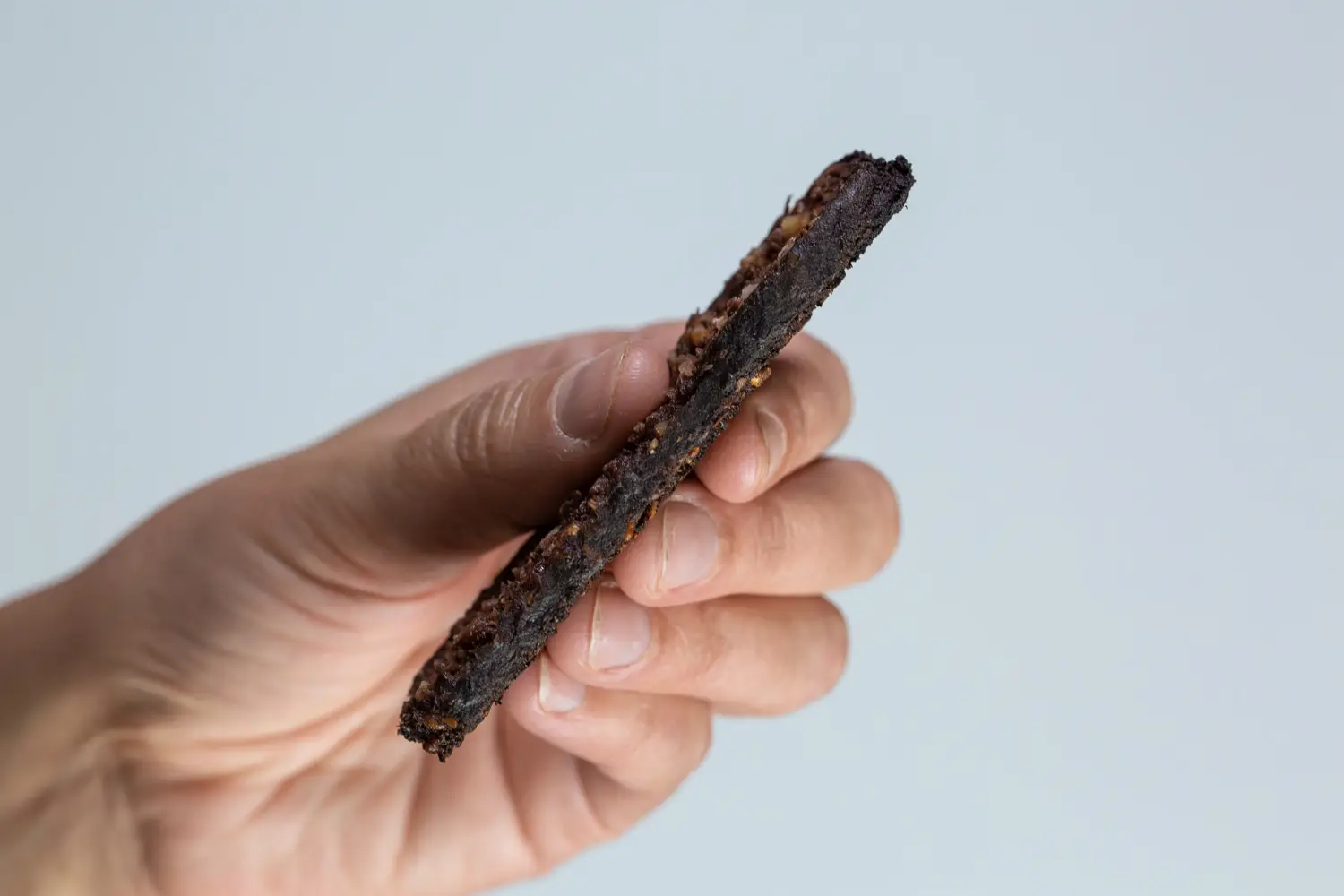 a hand holding a thin slice of blood sausage from the side to demonstrate how thin it is